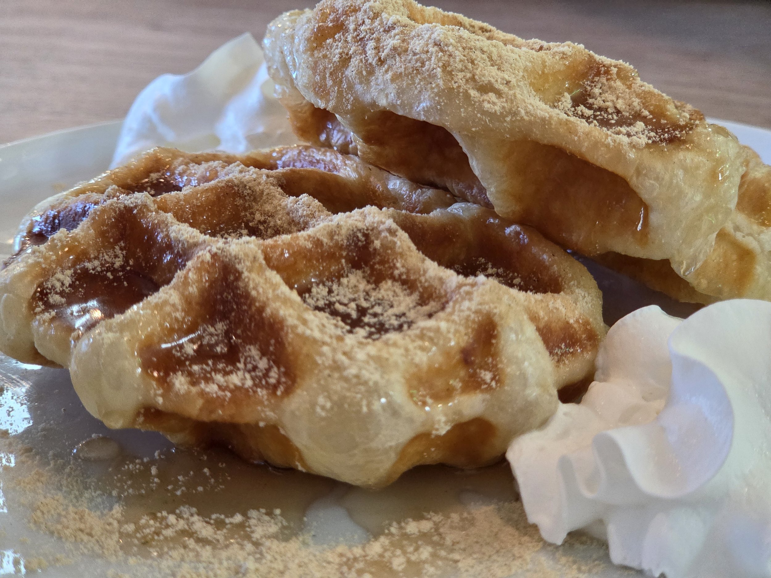 Two waffles dusted with powdered sugar, served on a white plate with whipped cream on the side.