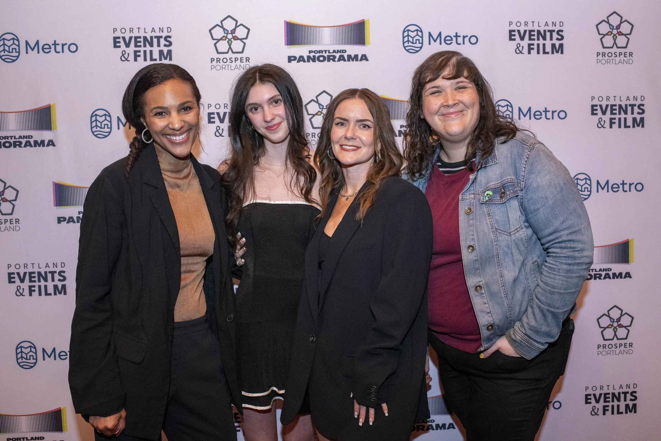 Four people standing on a red carpet in front of a backdrop with logos for Portland Events & Film, Portland Panorama, Prosper Portland, and Metro, smiling at the camera.