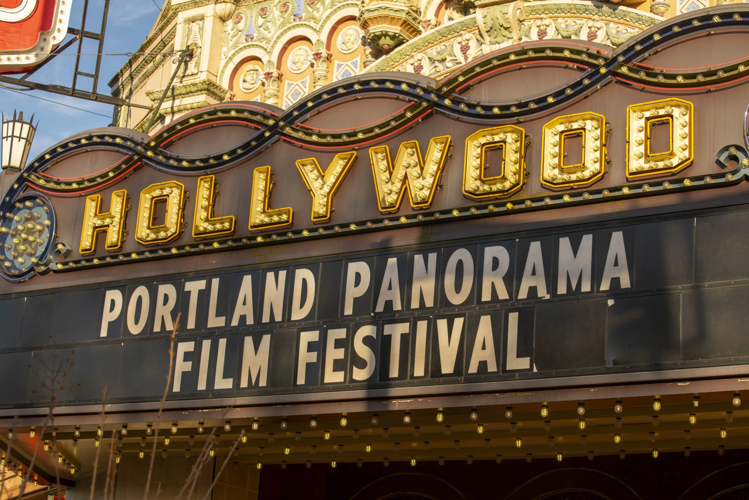 Marquee sign for the Portland Panorama Film Festival with the Hollywood sign above, illuminated with light bulbs in a vintage style, set against the background of a building with decorative columns and medallions.