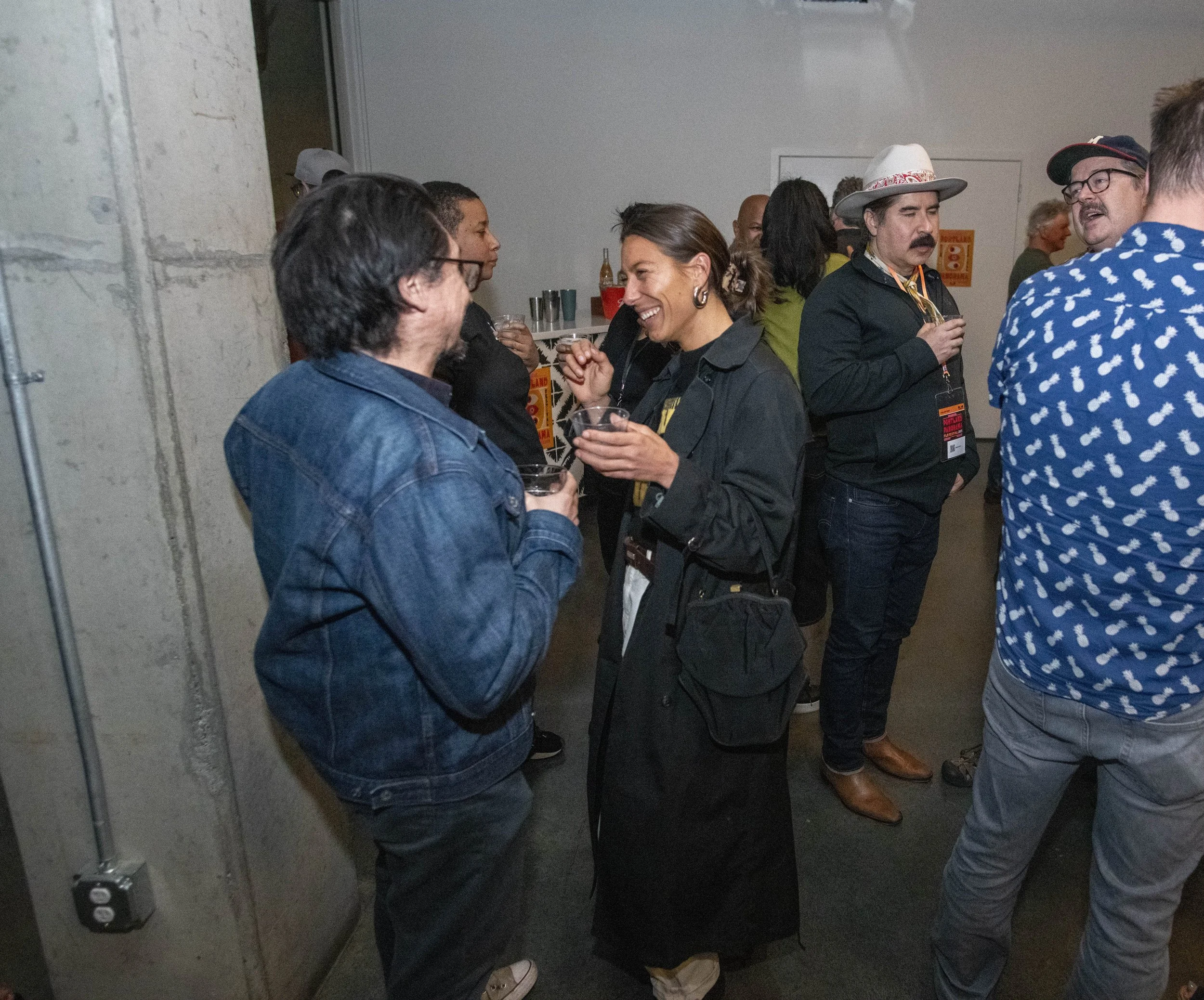 People socializing at an indoor event, engaging in conversation and holding drinks, with others in the background.