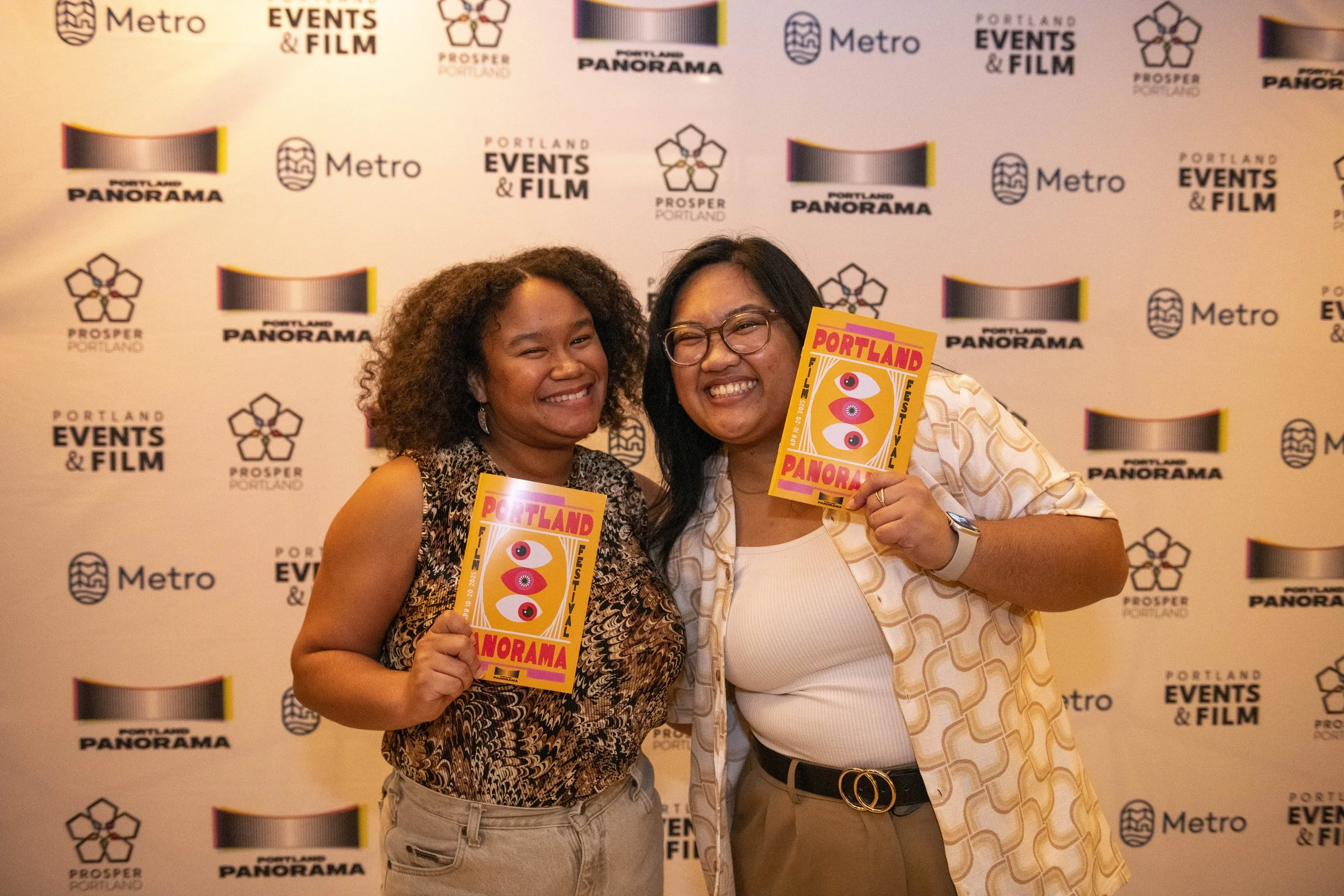 Two people smiling and holding festival flyers at Portland Panorama event, standing in front of a backdrop with Portland Panorama, Metro, and Portland Events & Film logos.