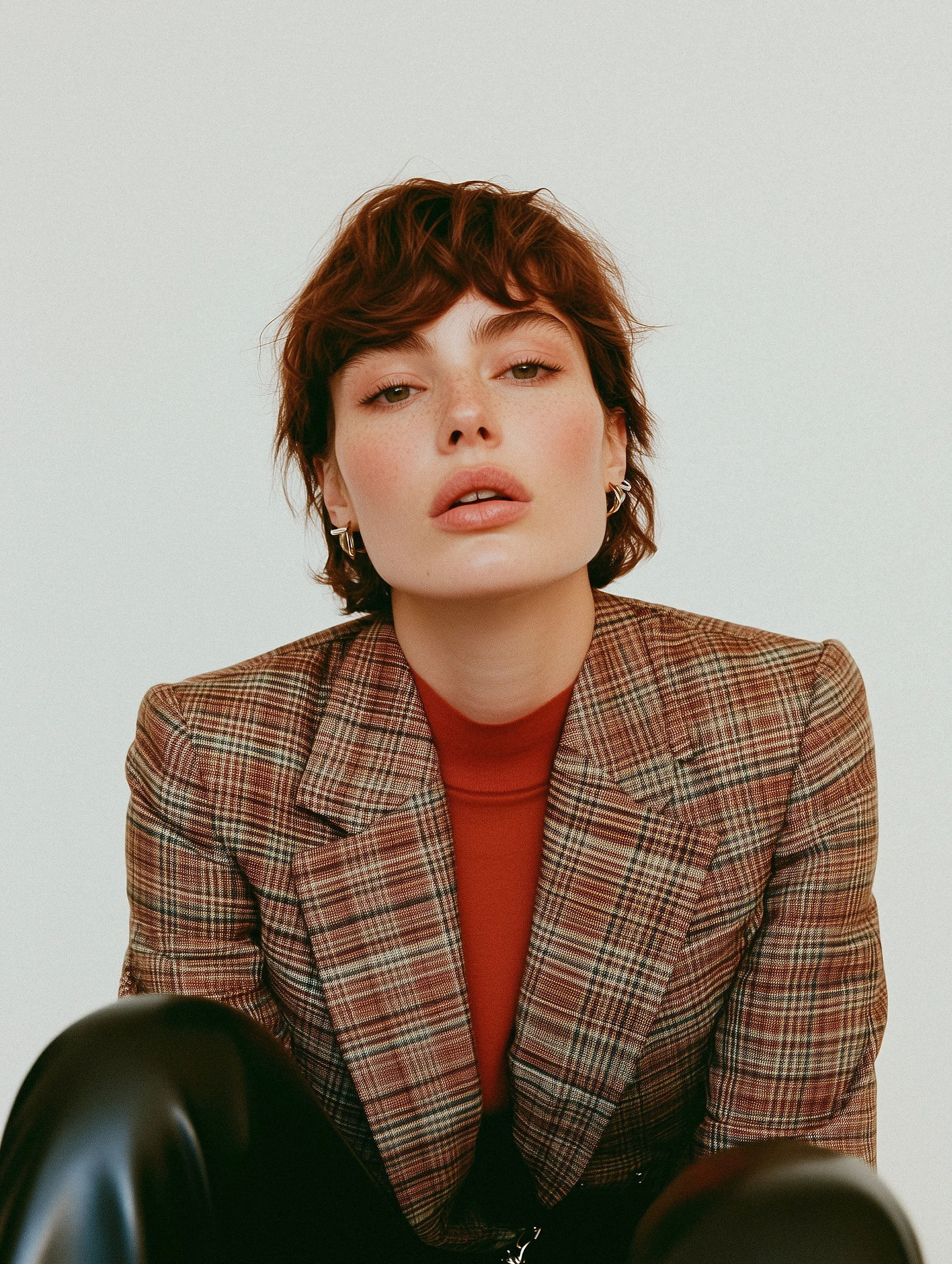 Person wearing a plaid blazer and red top with short brown hair looking at the camera.
