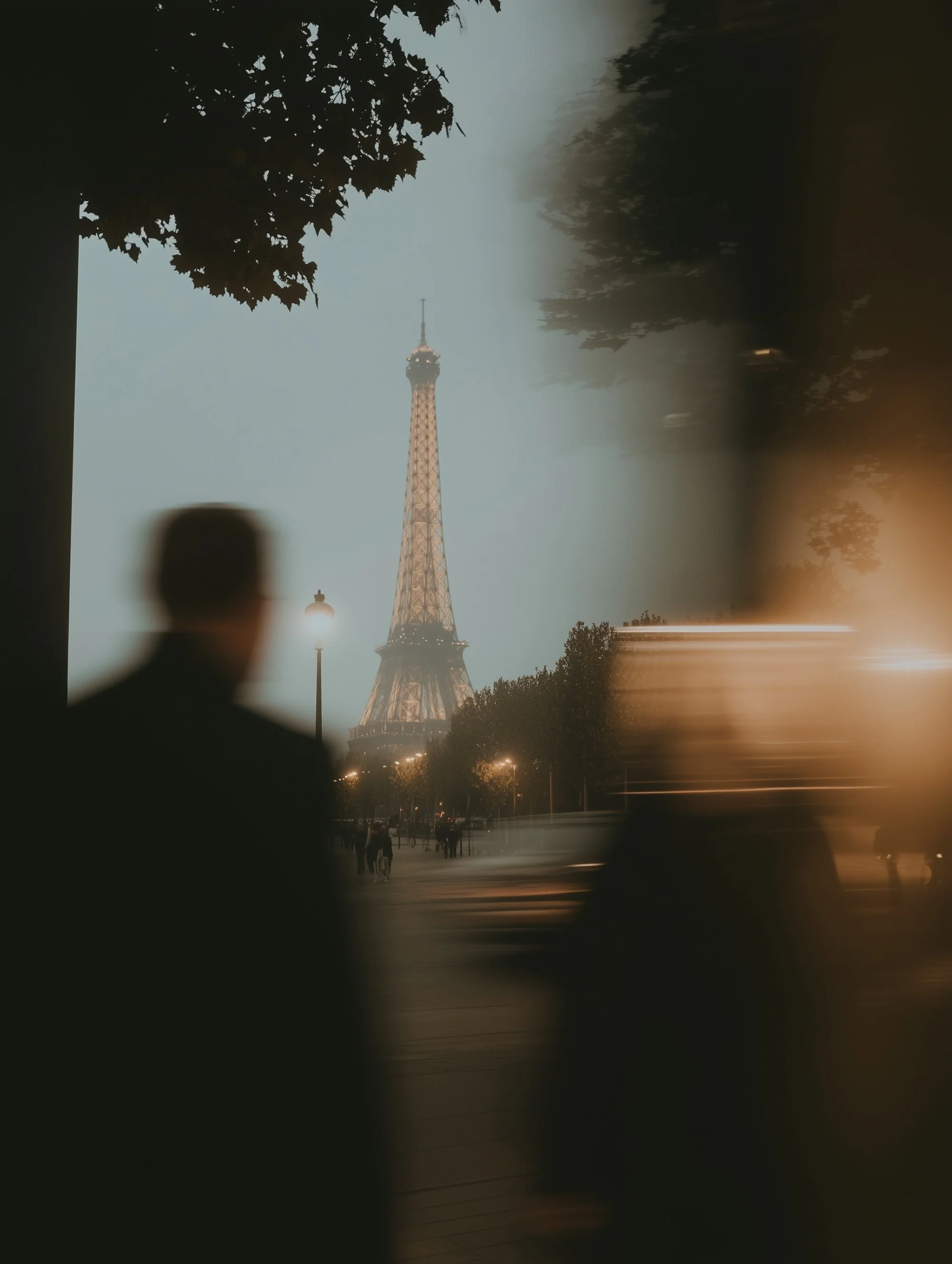 Eiffel Tower at night with blurred silhouettes and street lights in foreground.