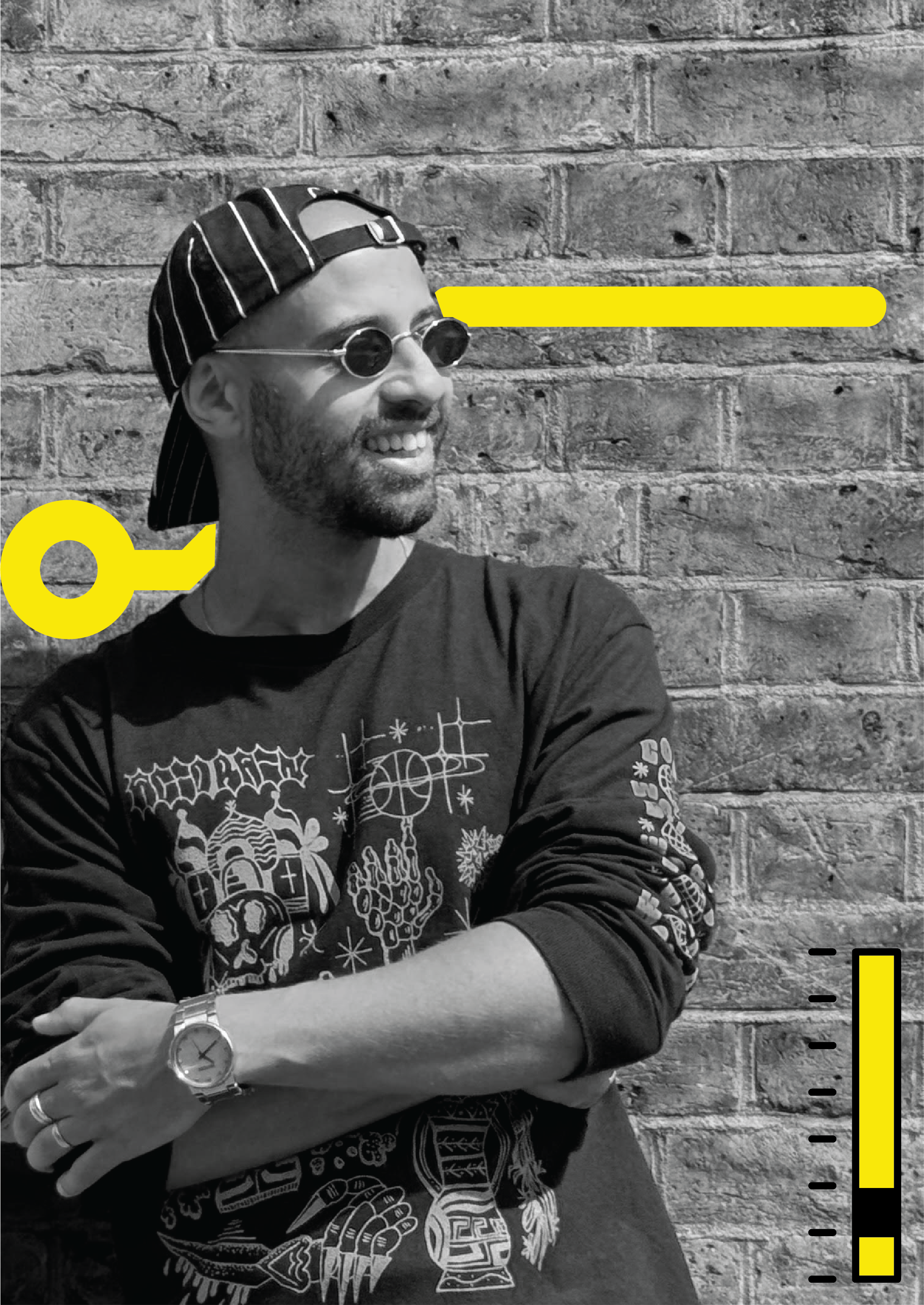Black and white photo of a smiling man wearing round sunglasses, a backwards striped cap, a watch, and a long sleeve shirt with graphic designs, standing against a brick wall.
