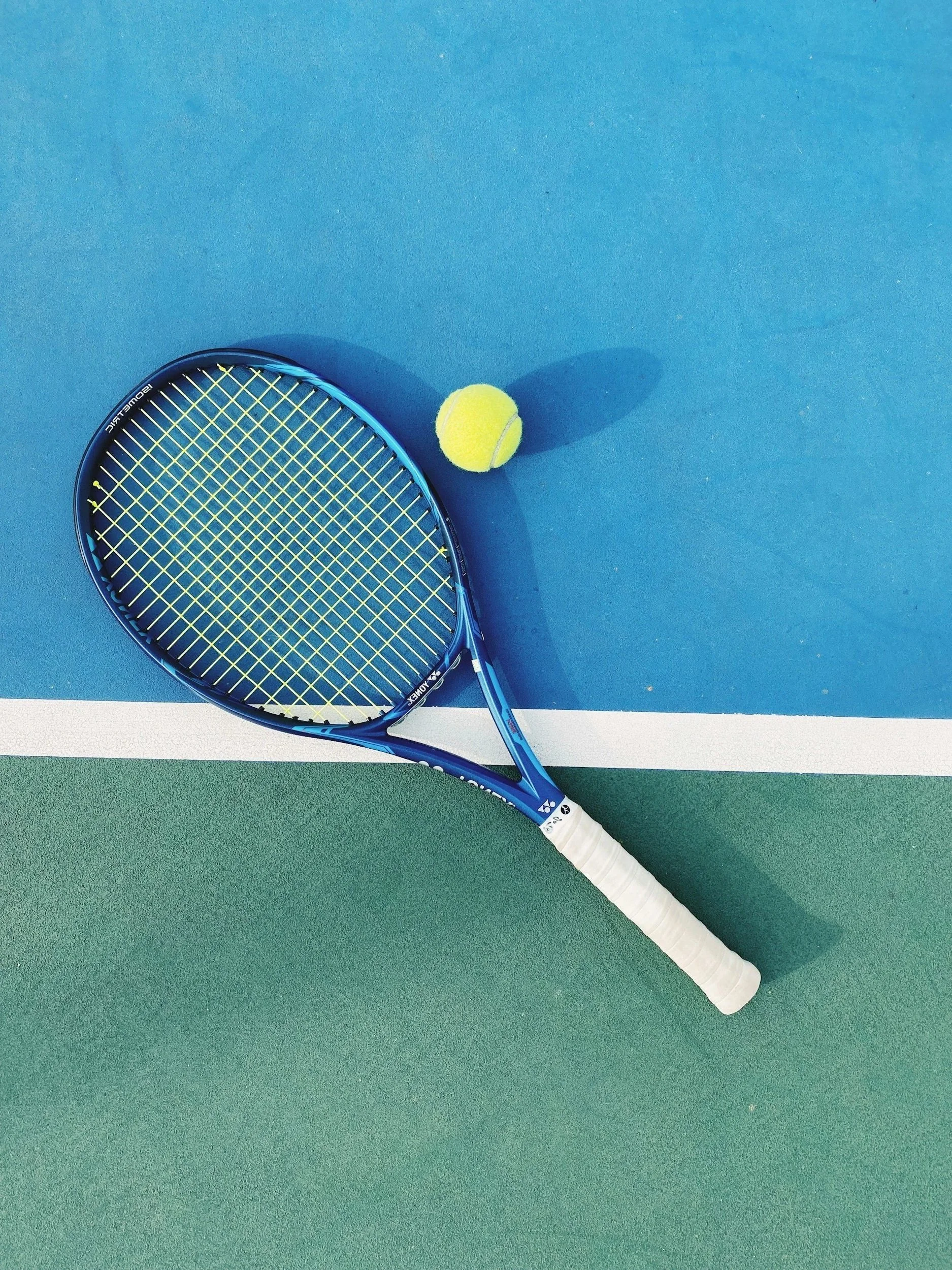 Tennis racket and yellow tennis ball on a blue and green tennis court.