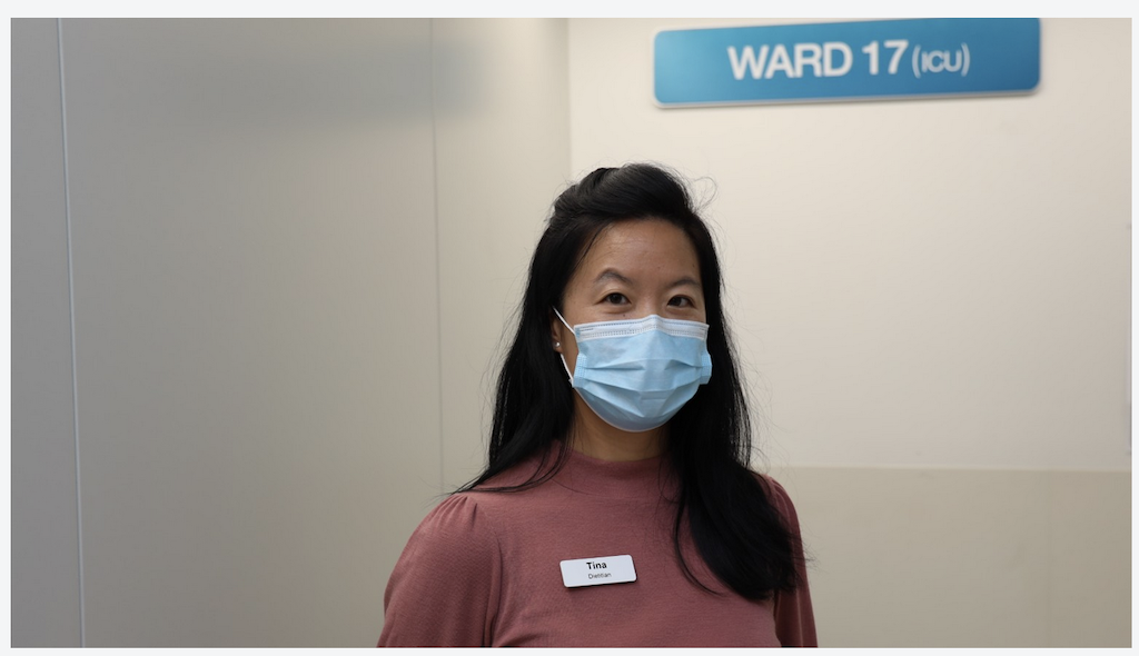 A woman wearing a face mask and a name tag that says 'Tina' stands in front of a hospital room sign labeled 'WARD 17 (ICU)'.
