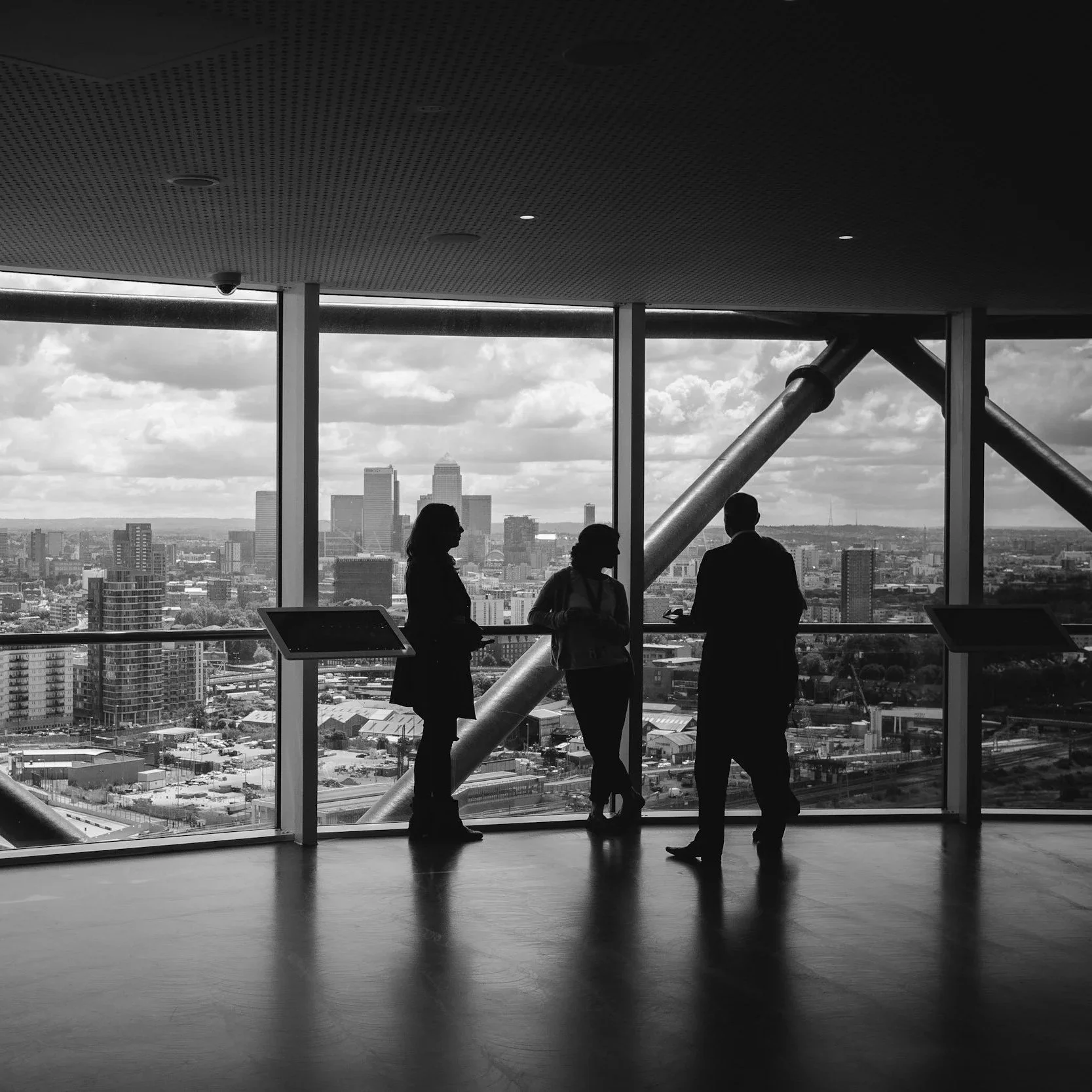 Silhouettes of three people having a conversation inside a high-rise building with a city skyline view through large windows in the background.
