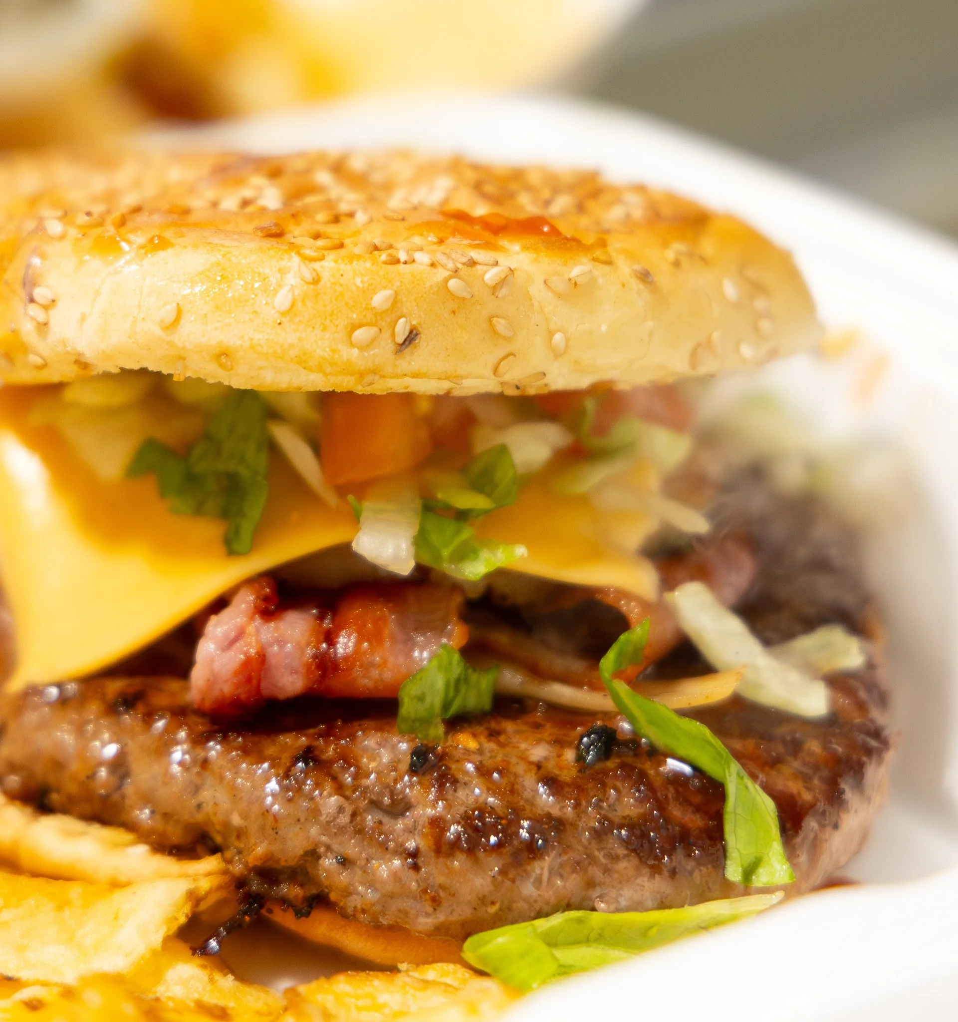 Close-up of a cheeseburger with lettuce, bacon, and sesame seed bun.