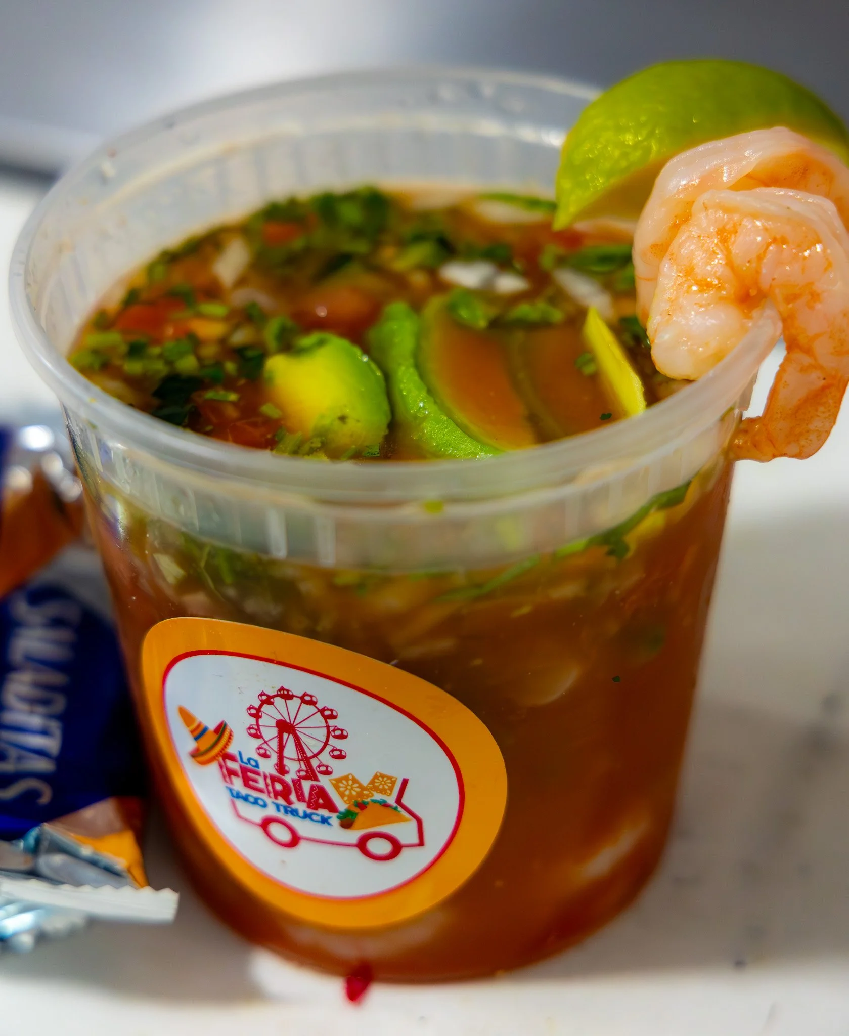 A cup of shrimp cocktail with lime wedge and chopped vegetables in sauce, with a "La Feria Old Town" logo on the cup.