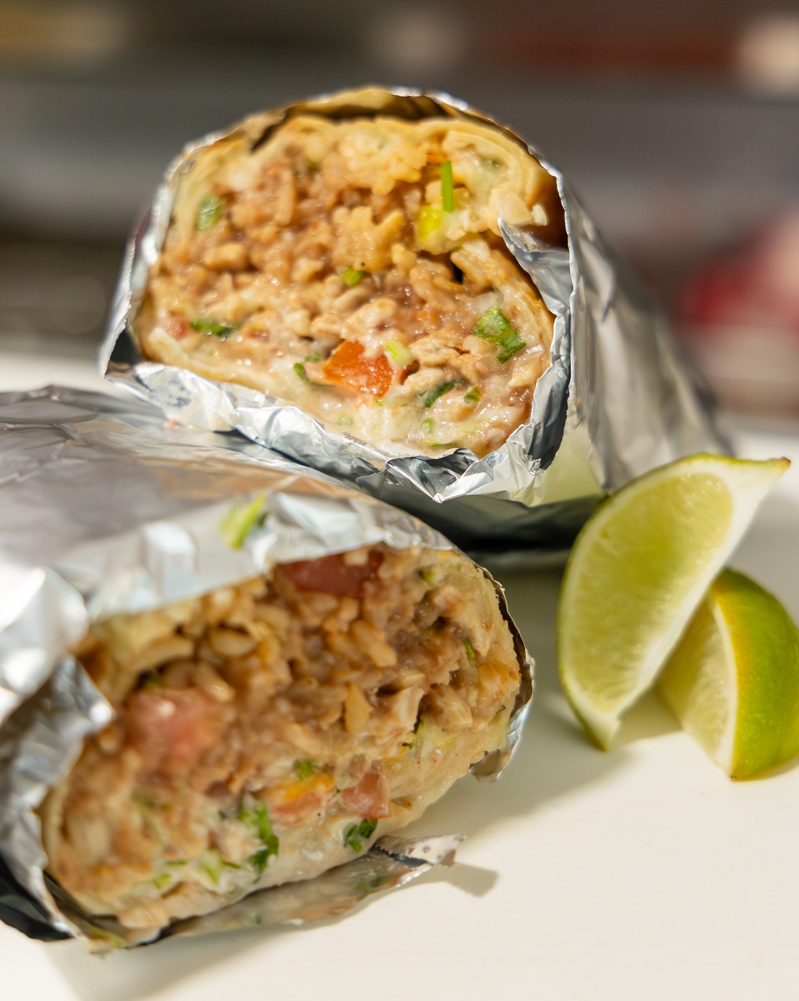 Close-up of two partially unwrapped burritos with a side of lime wedges.