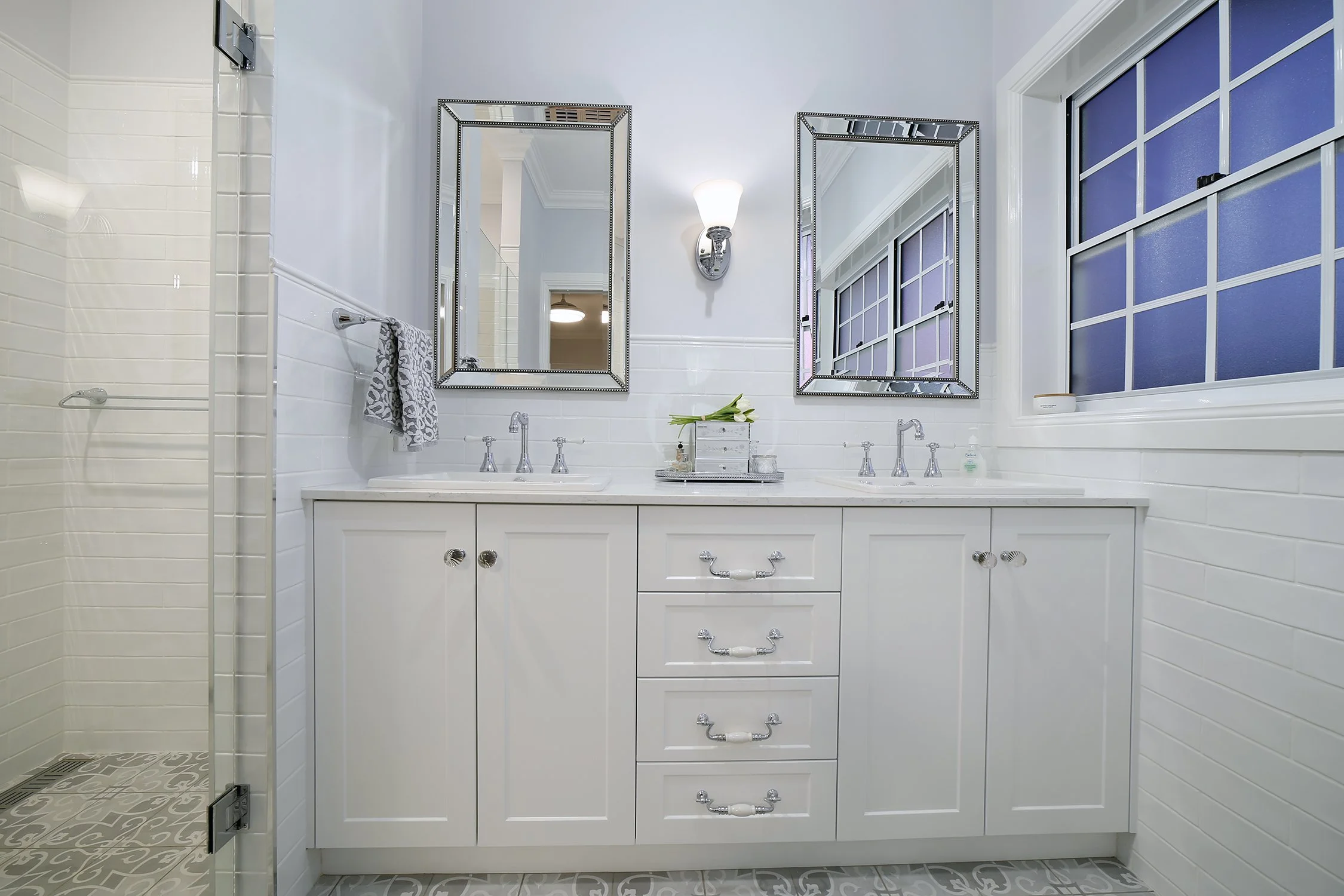 Double vanity bathroom with white cabinets, two mirrors, two sinks, a towel, and a window with frosted glass.