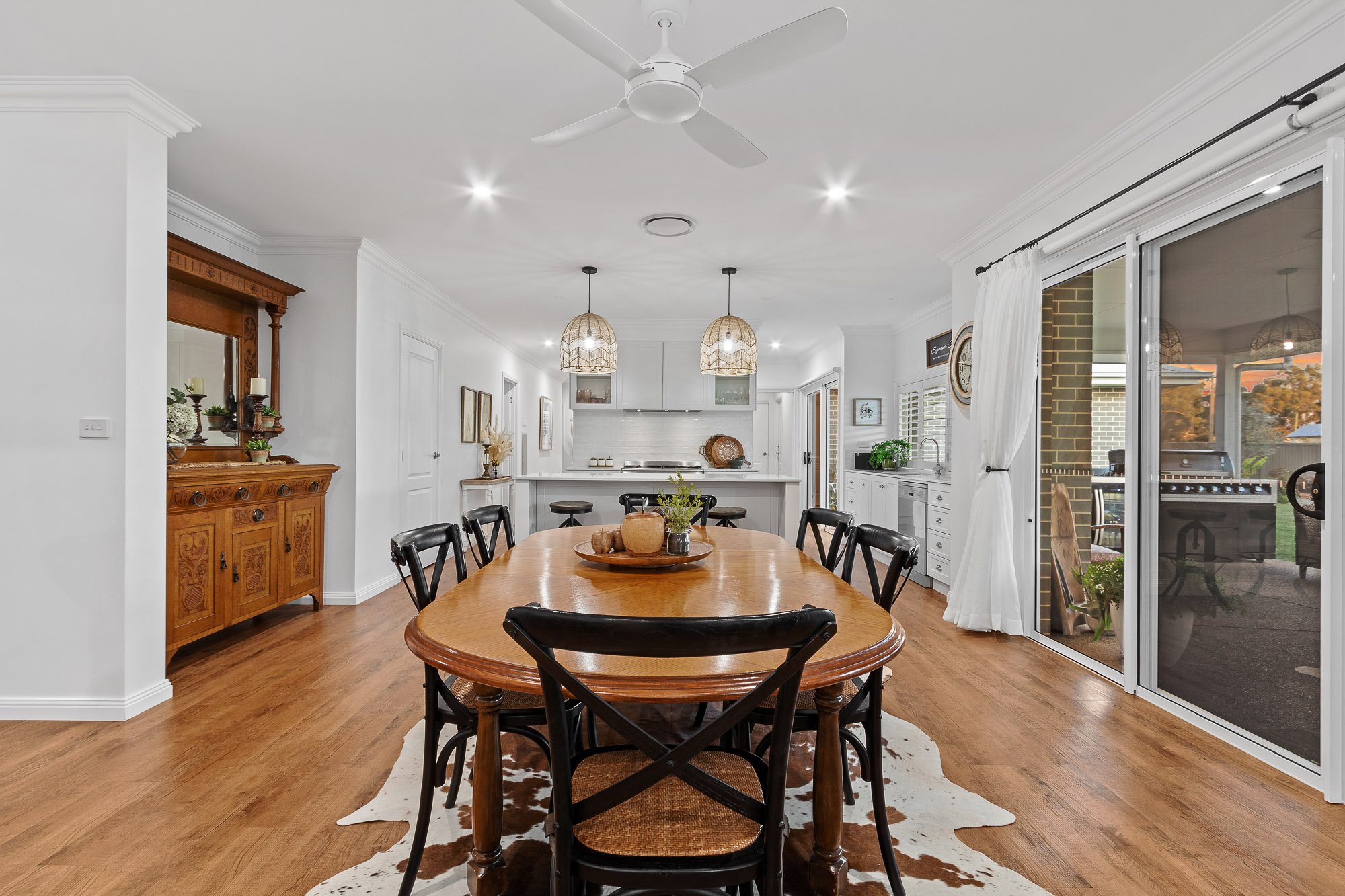 Dining room with wooden table, black chairs, white walls, ceiling fan, and sliding glass doors to patio with outdoor grill.