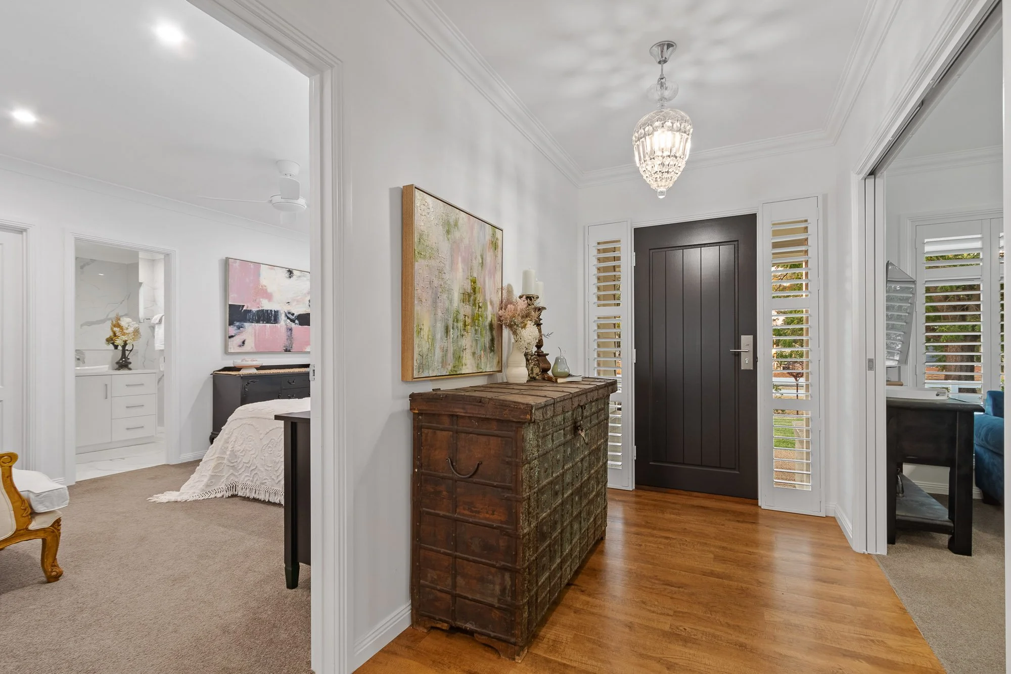 Entryway with dark front door, wooden chest with decorative items, chandelier, and white walls with crown molding.