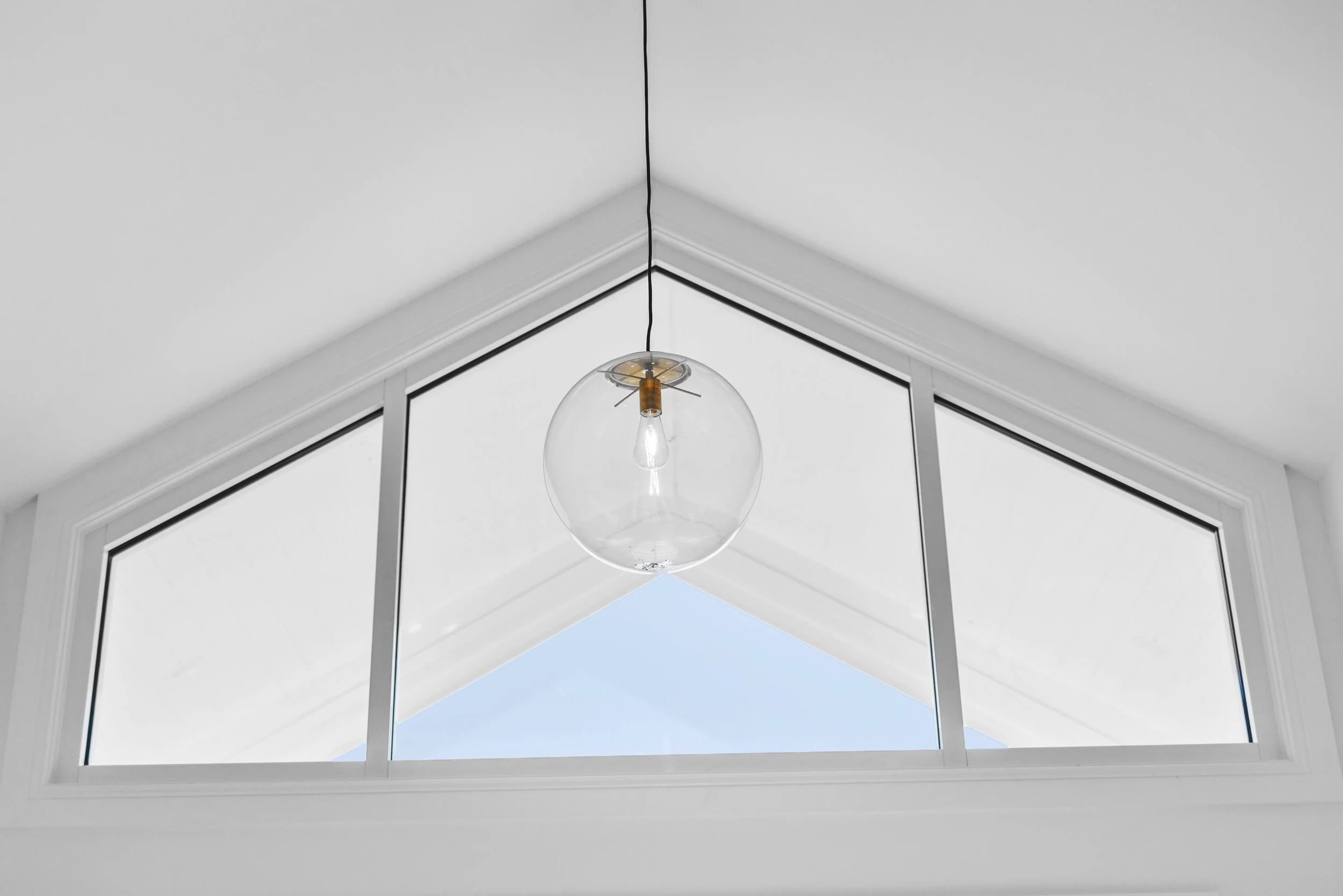 Modern interior ceiling with a triangular window and a hanging clear glass globe light fixture.