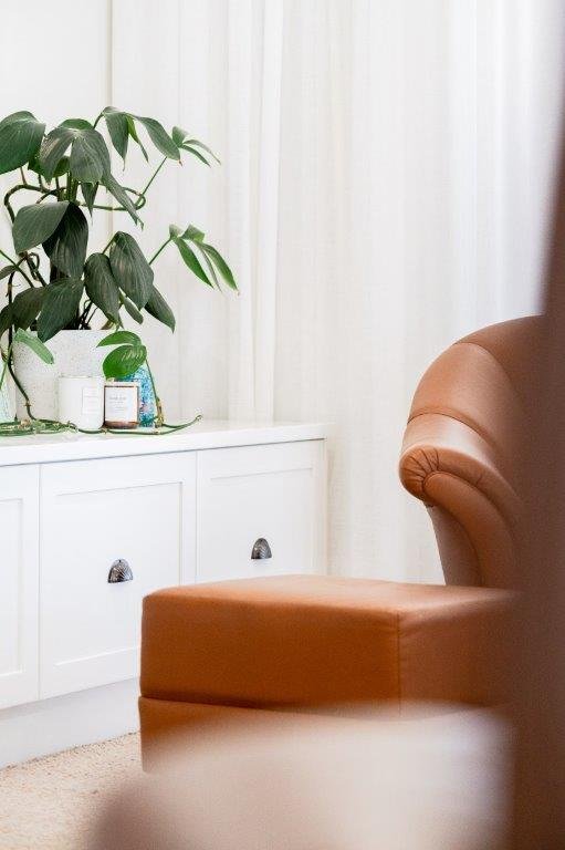 Living room corner with a white cabinet, a large green houseplant, a brown armchair, and beige curtains.