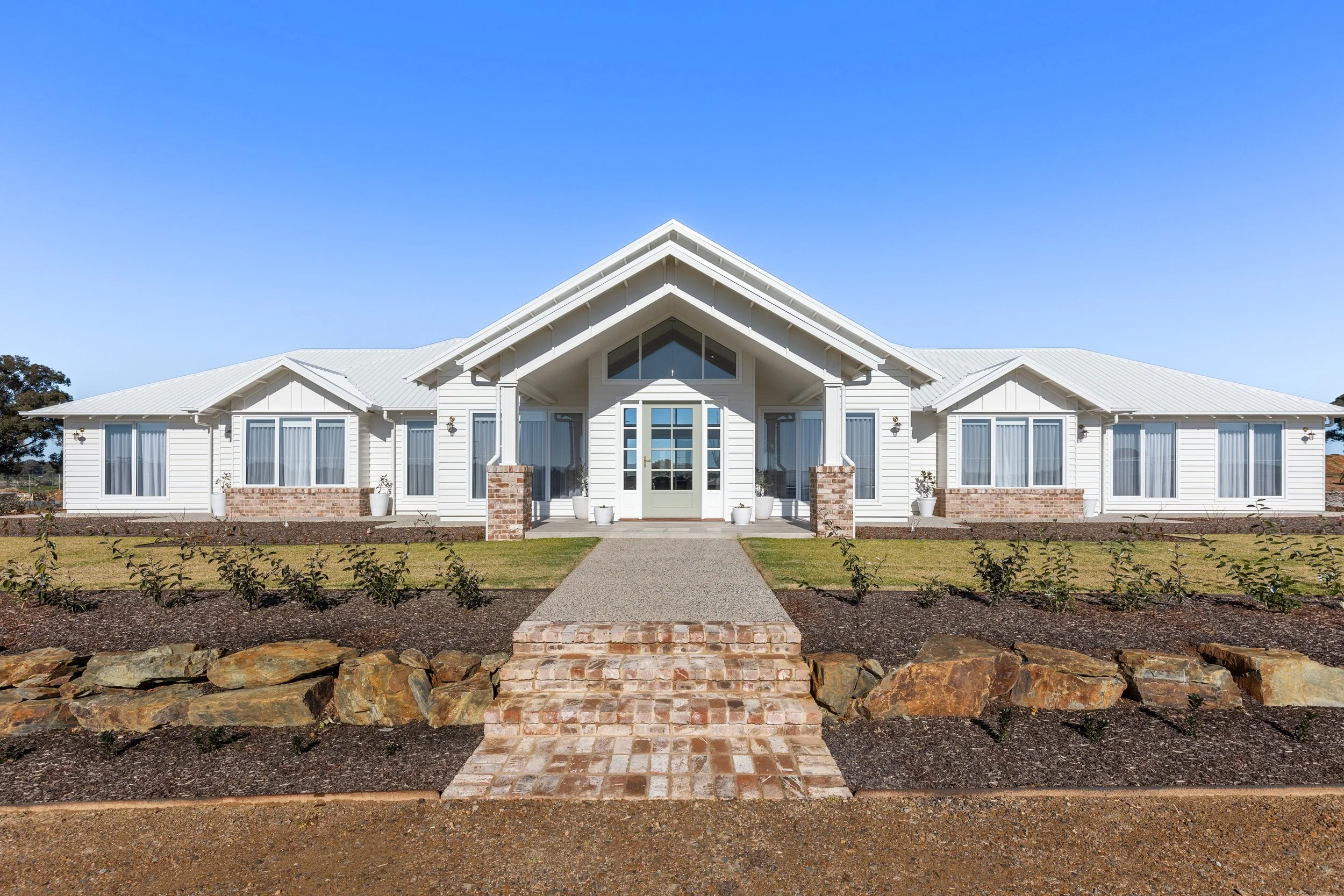 Front view of a large white house with a brick pathway and landscaped yard.