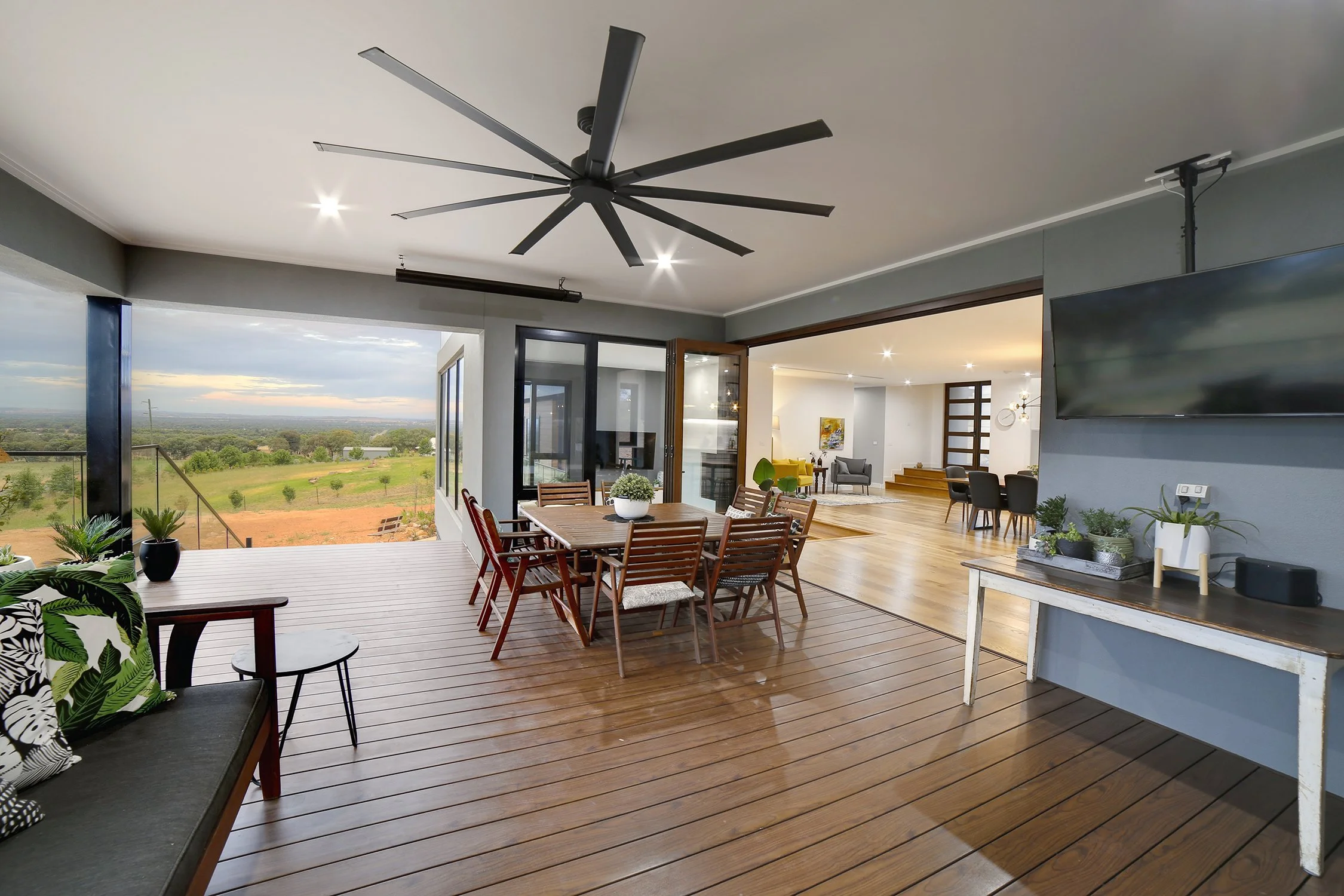 Open-concept living and dining area with wooden floors, a ceiling fan, large windows showing a scenic outdoor view, and modern furniture.