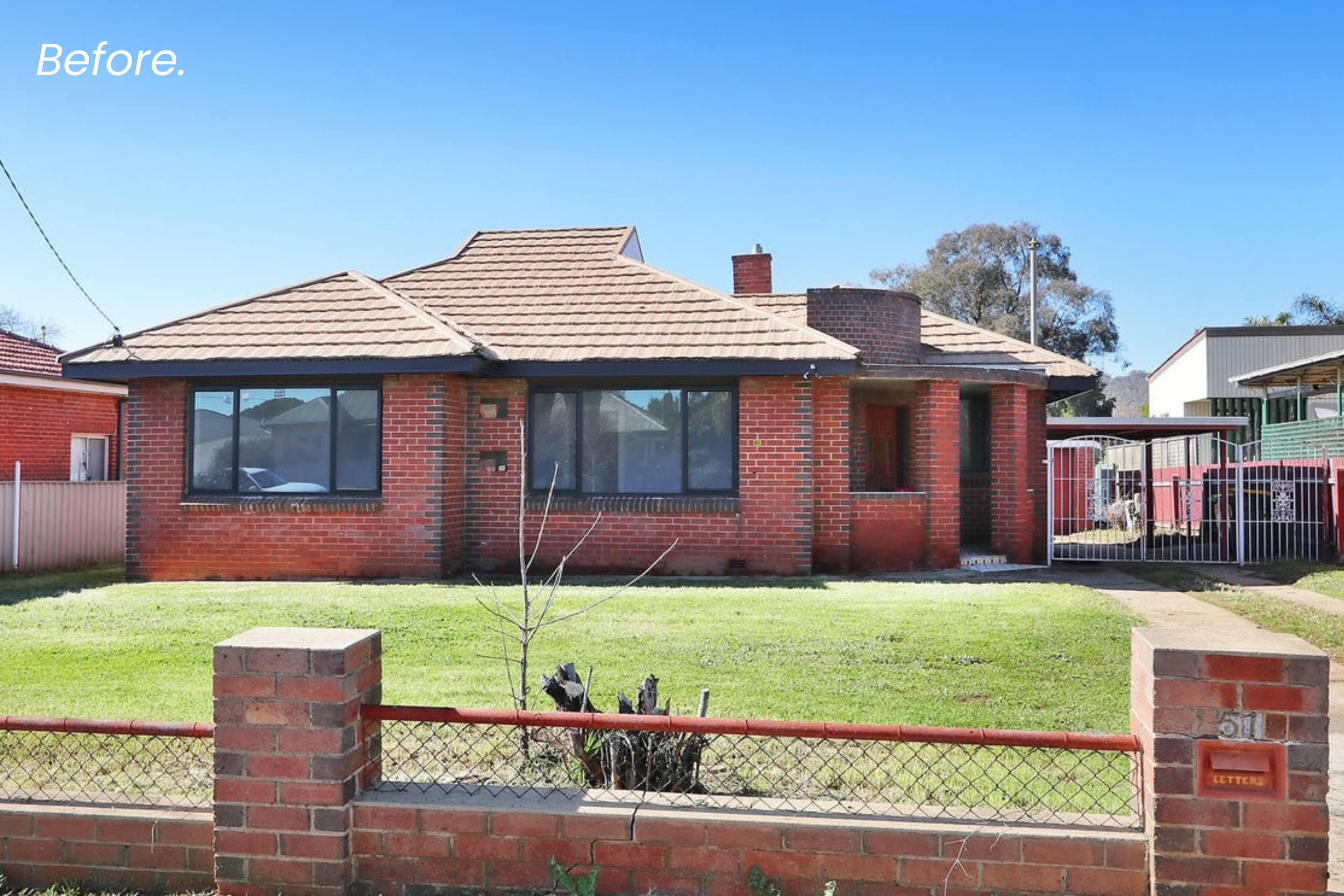 Front view of a red brick house with large windows, a fenced yard, and a small tree with burn marks on the lawn, under a clear blue sky.