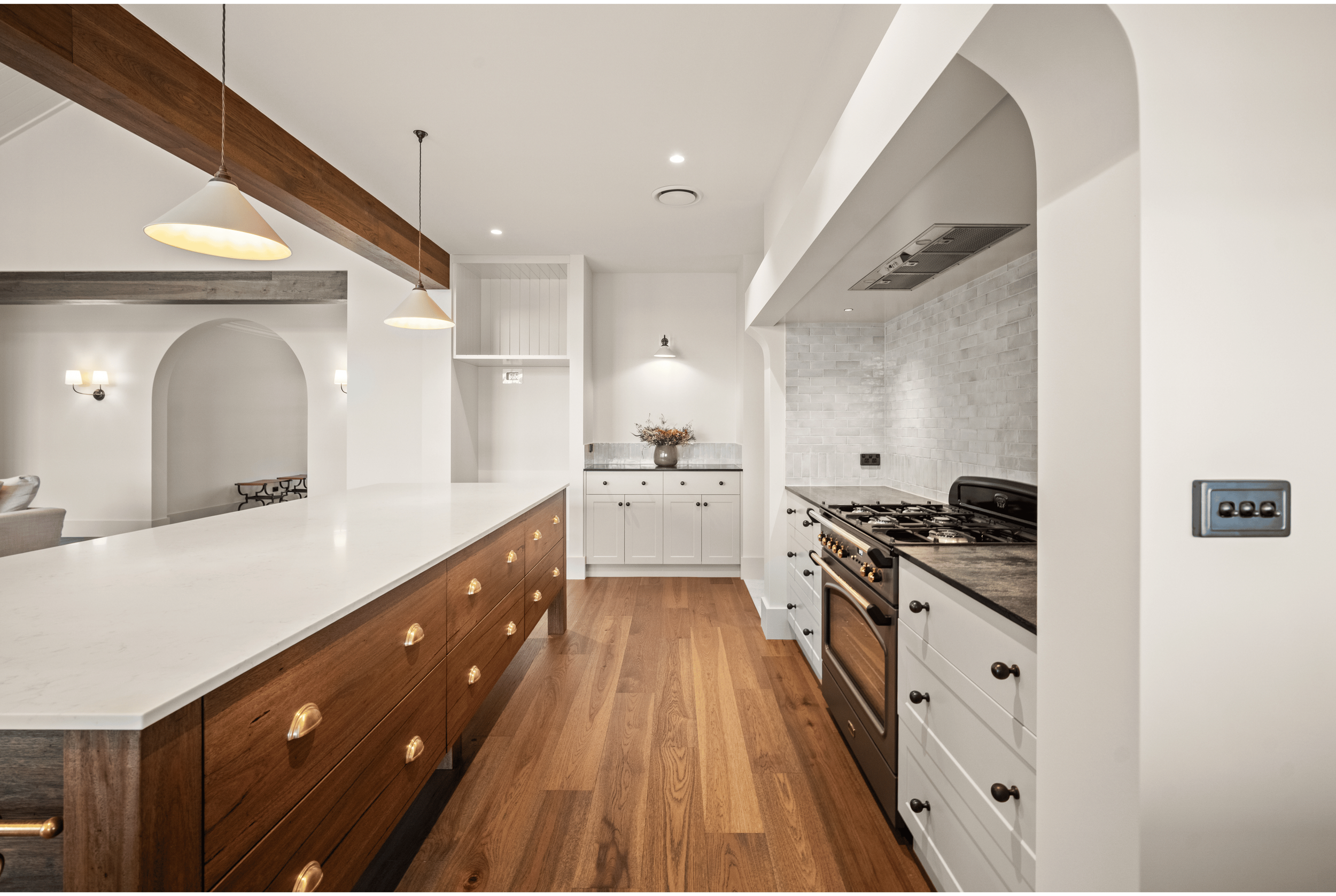 A modern, bright kitchen with white cabinets, marble island and backsplash, large windows, and wood flooring.