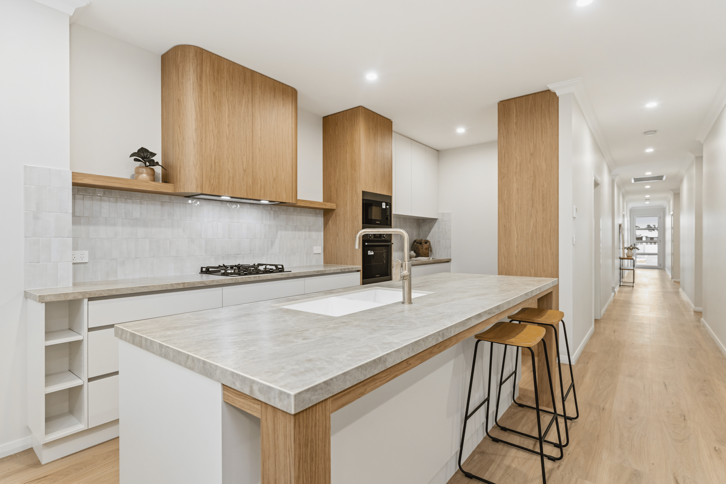 Modern kitchen with white marble island and cabinetry, large windows and glass doors leading to an outdoor view of fields and trees, high vaulted ceiling, hardwood floors, and natural sunlight.