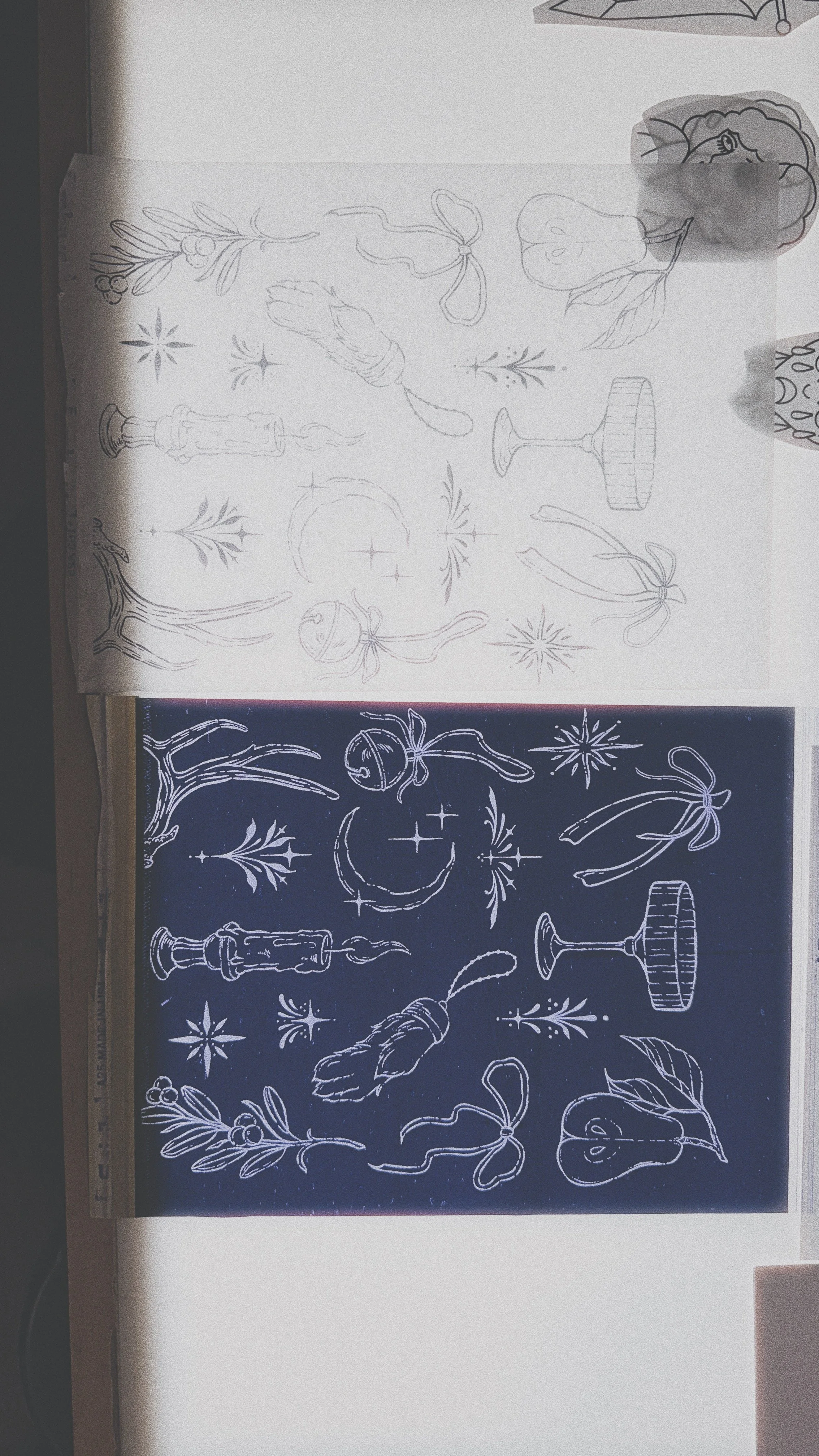 Line drawing of holiday decorations, including candles, ribbons, stars, leaves, bells, and a mistletoe branch, antlers, and champagne coupe on a piece of separated tattoo stencil paper.
