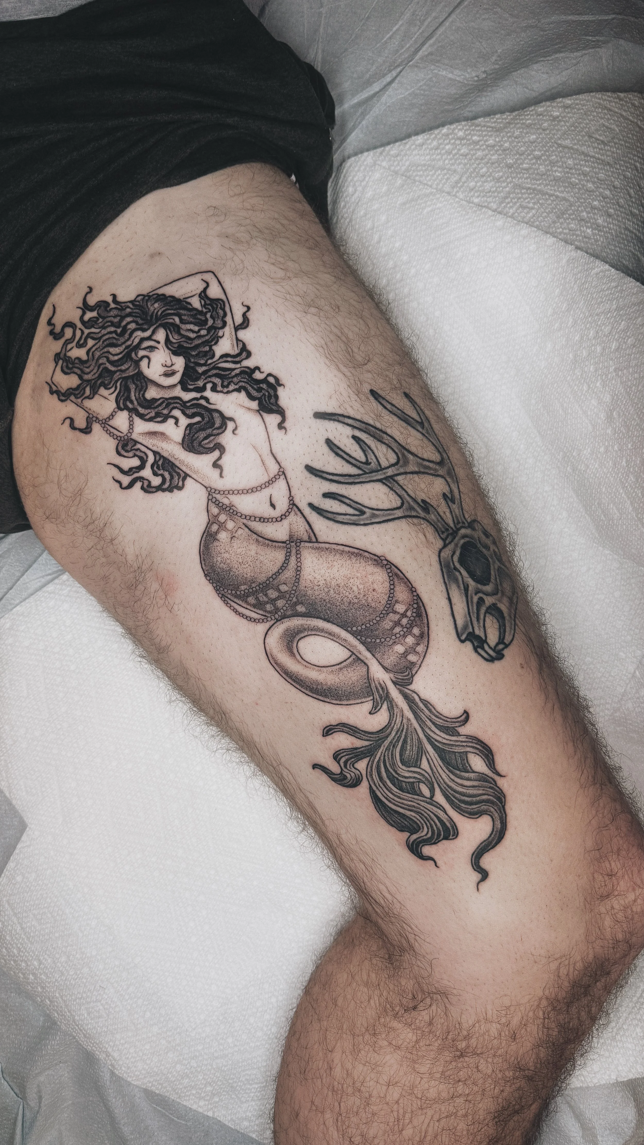 blackwork dotwork illustrative siren with flowy hair and tail with pearls draped around her. large full thigh tattoo