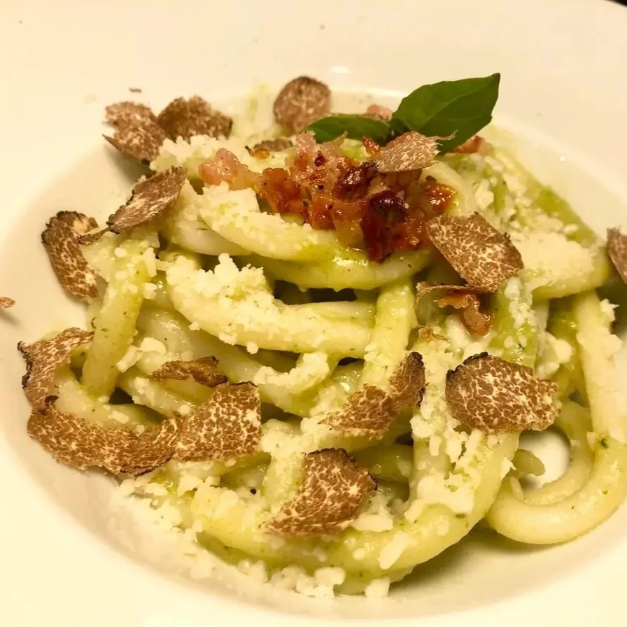 Close-up of pasta with truffle slices, grated cheese, and a small amount of tomato sauce topped with a basil leaf.