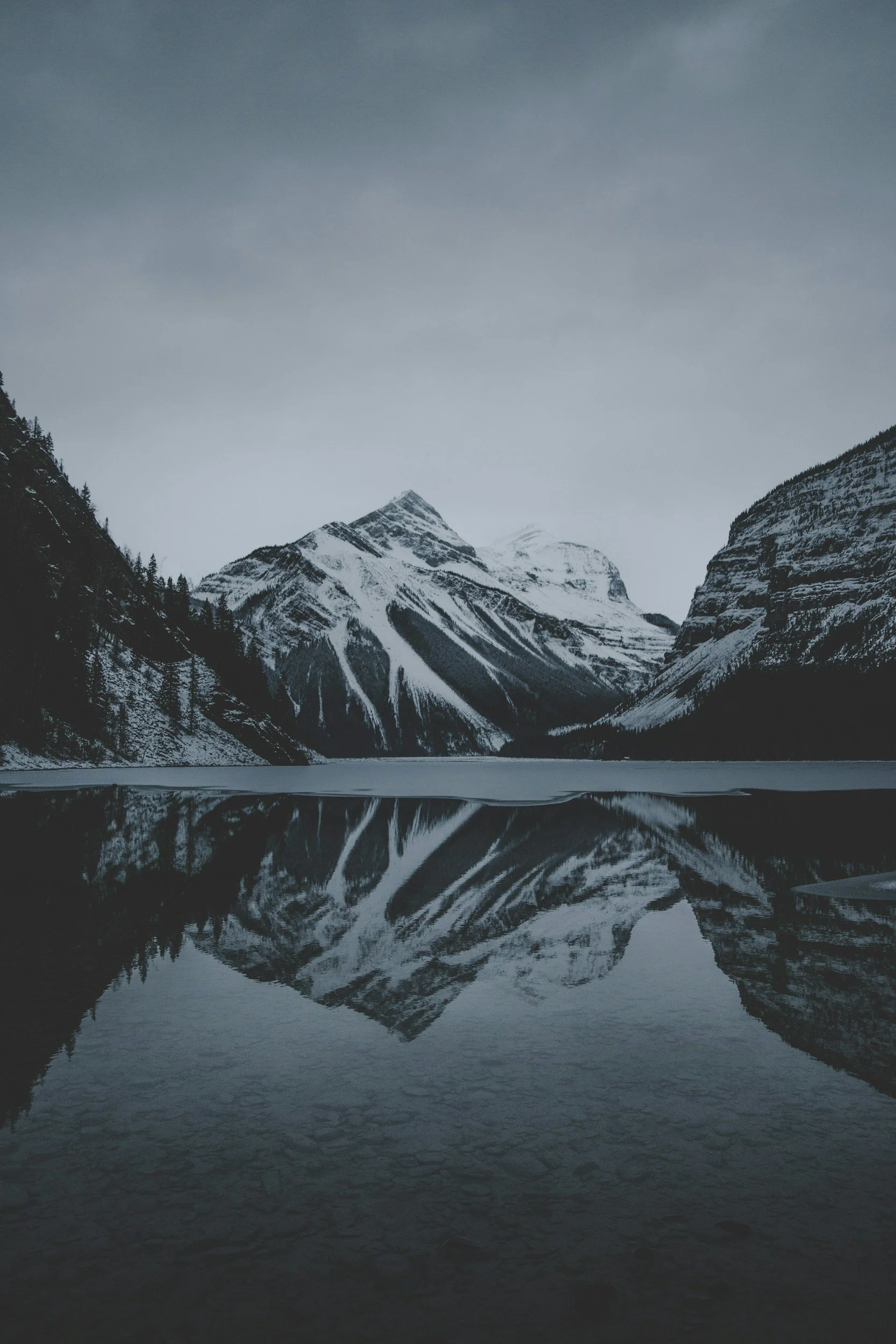 Snow-capped mountains reflected in a calm lake with moody, overcast sky