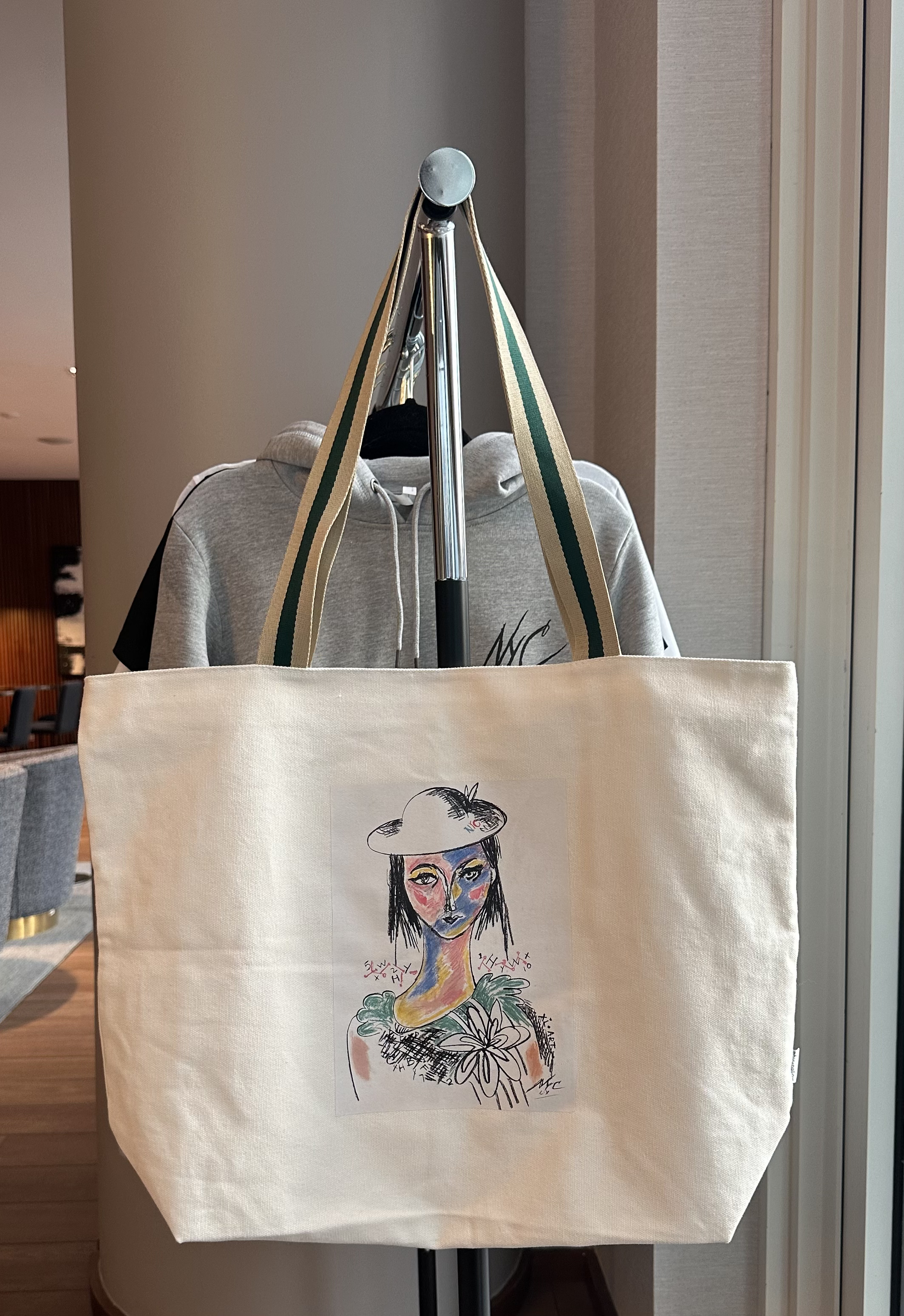 A tote bag with a colorful artistic drawing of a woman with long dark hair, a hat, and a large flower on her chest.