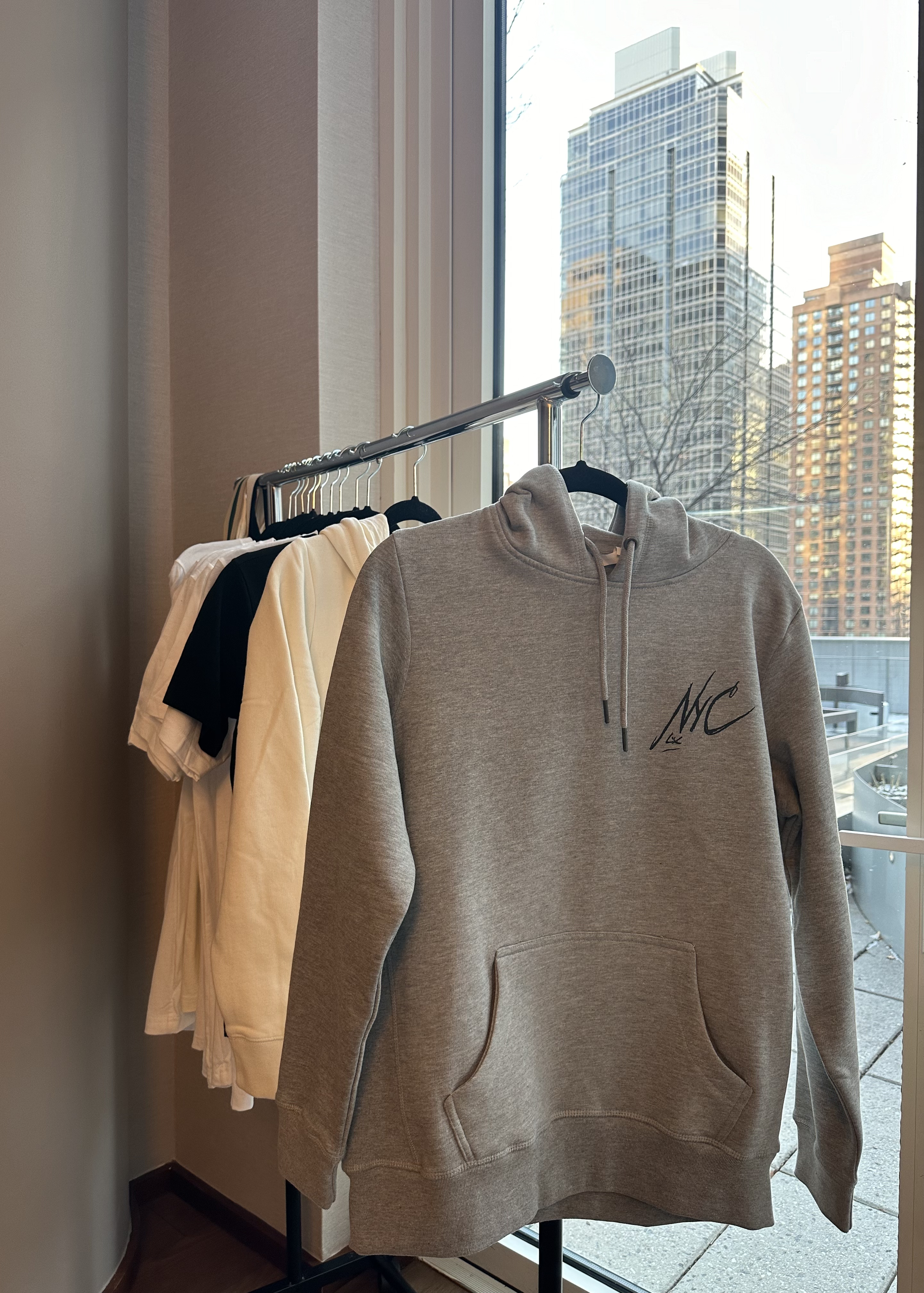 Display of clothes on a clothing rack by a large window with city buildings outside, including a tall modern glass building.