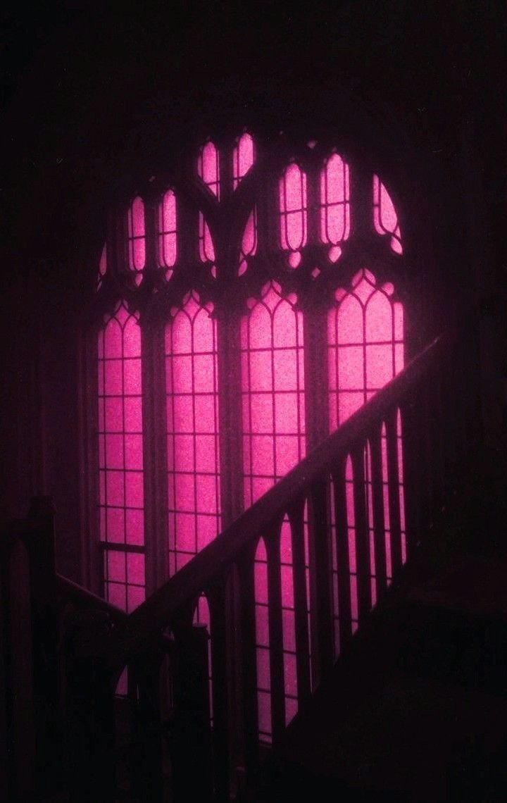 Pink stained glass window with gothic arches, viewed through a dark staircase railing.