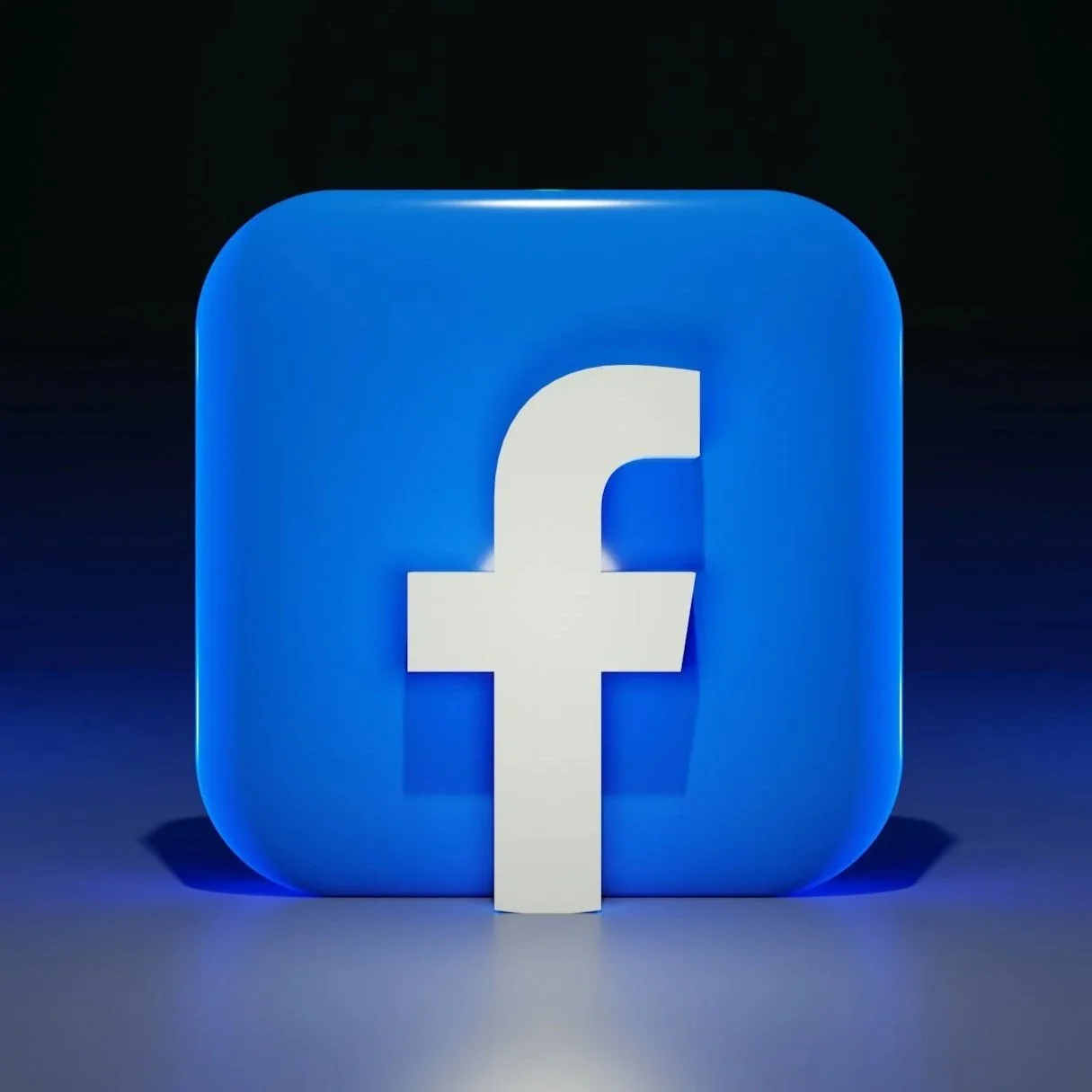 A large 3D Facebook logo with a white letter 'f' on a blue rounded square background, illuminated with blue lighting in a dark setting.