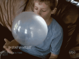 A young boy sitting on a couch looking at a large, transparent balloon.