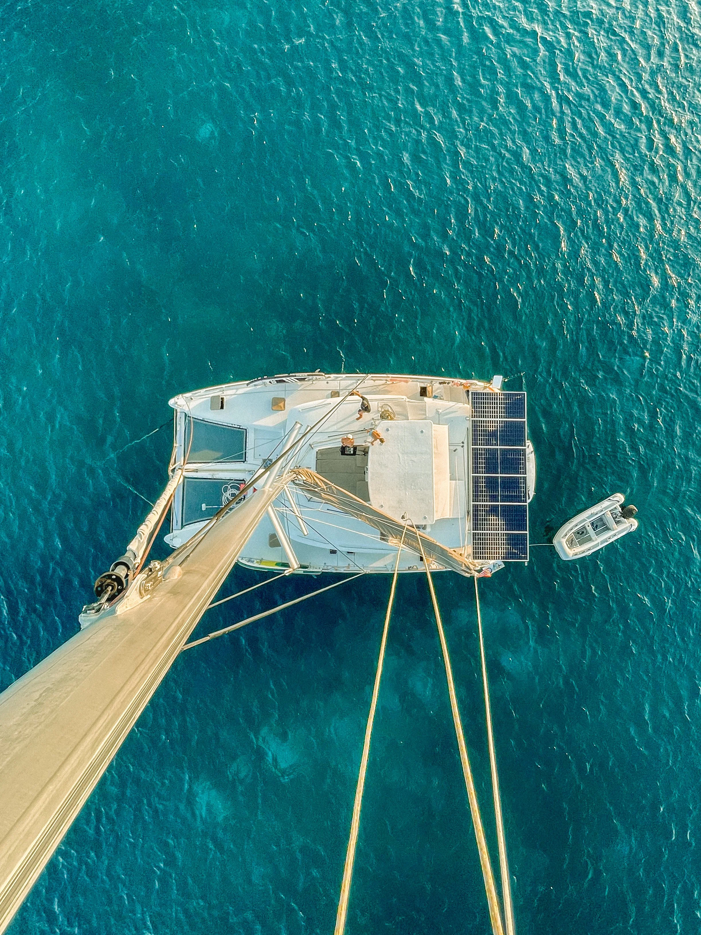 View from above of a sailboat with solar panels, floating on blue ocean water, with a small motorboat nearby.