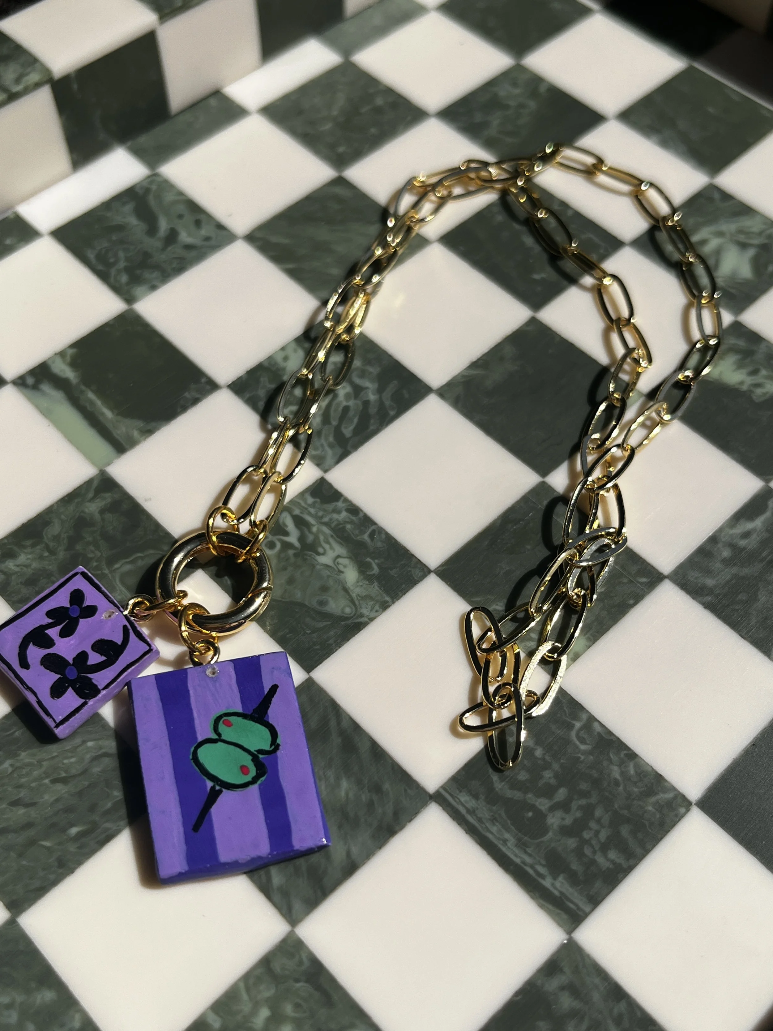 A gold and silver chain necklace with three colorful charms on a black and white checkered surface.