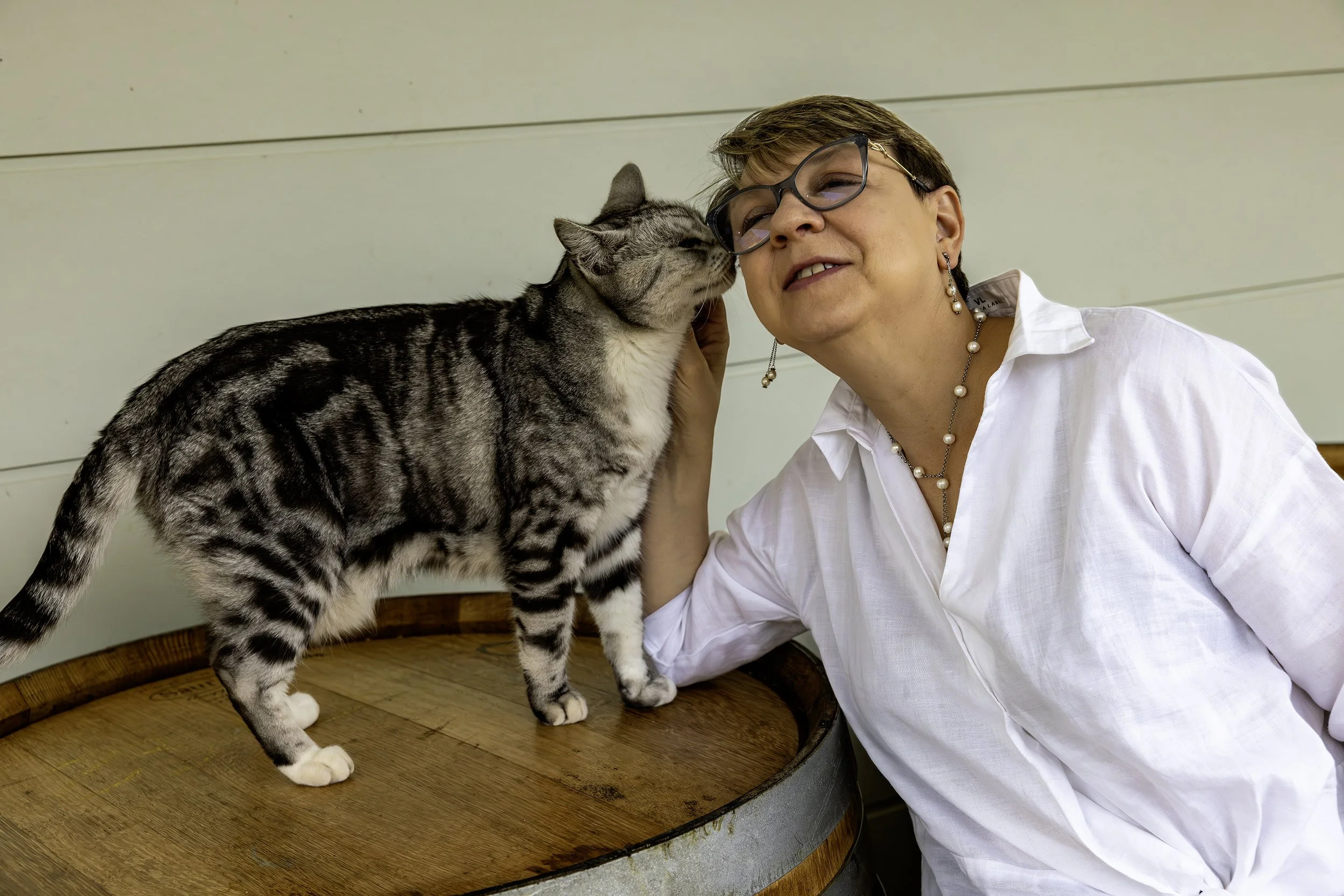 Pet photographer sharing a playful moment with a gray tabby cat leaning against a wooden barrel