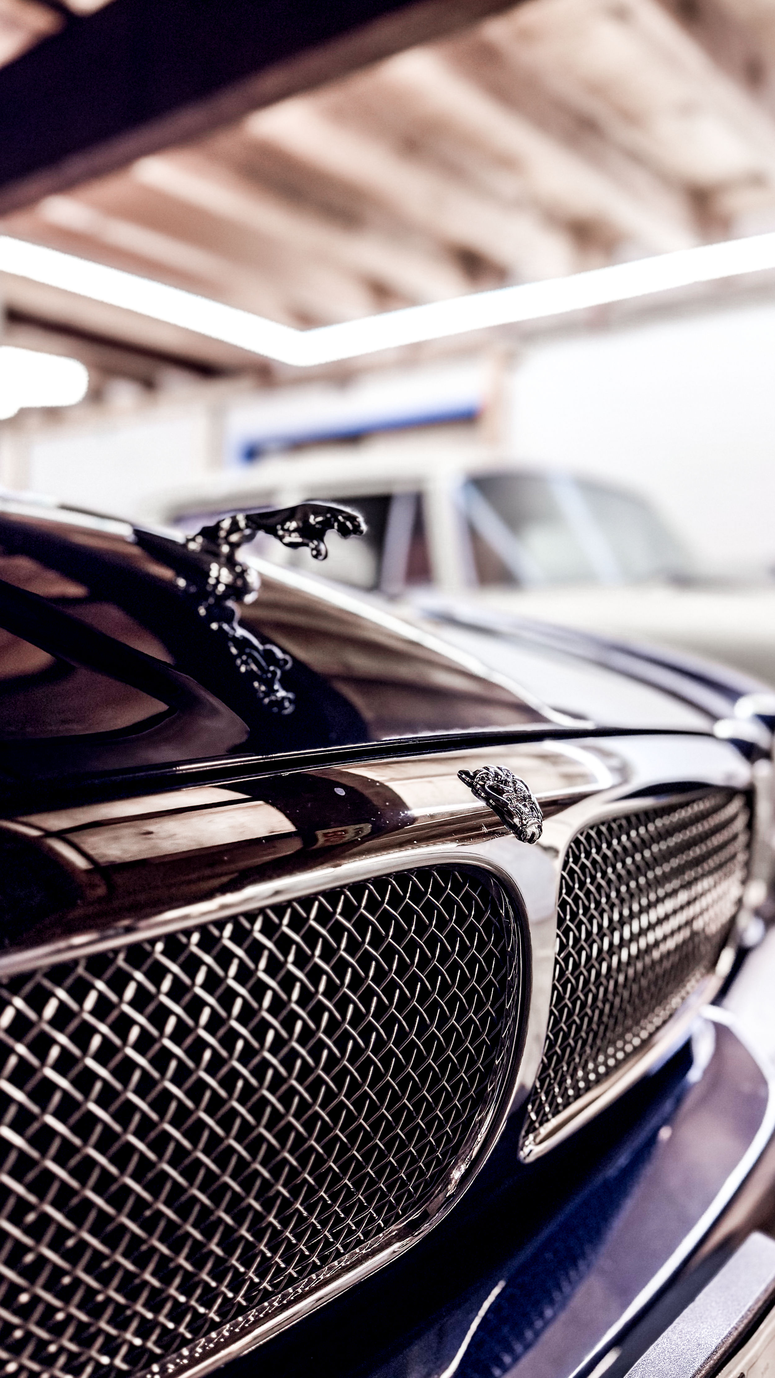 Close-up of a vintage black car with chrome grille and hood ornament, parked in a garage with wooden roof beams in the background.