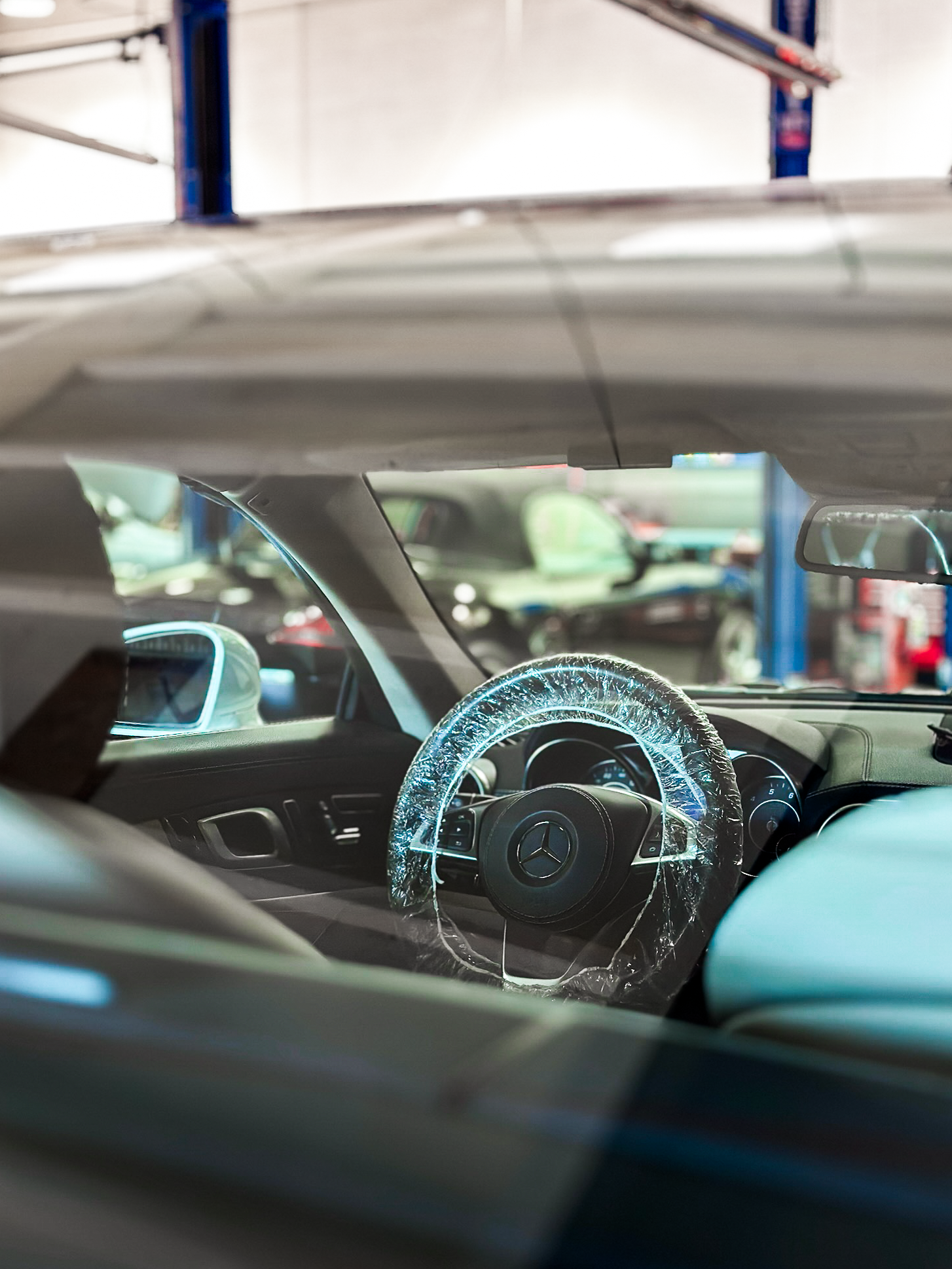 Interior view of a damaged Mercedes-Benz car with a cracked steering wheel cover, seen through the windshield at a repair shop.