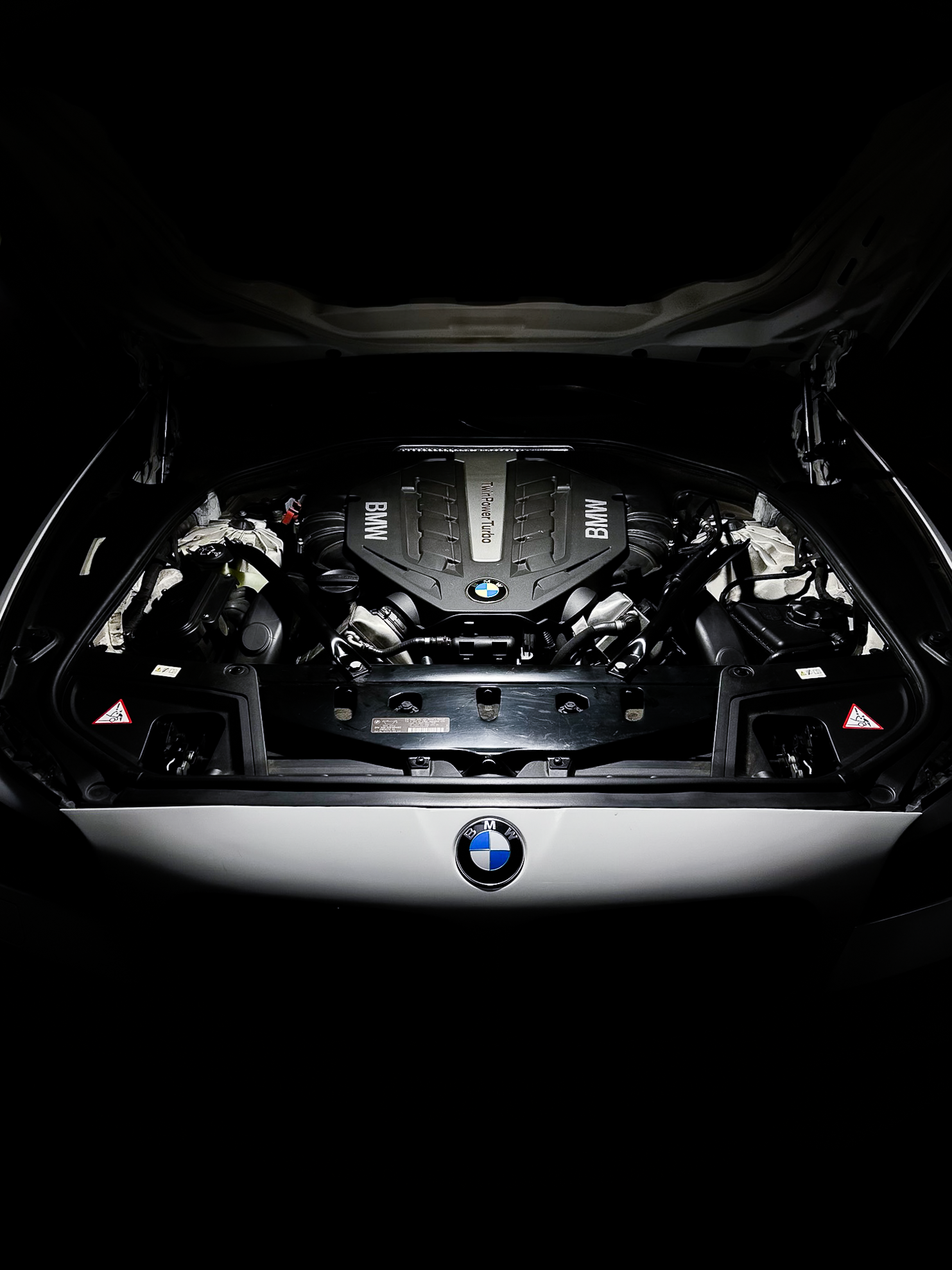 Under the rear hatch of a BMW car, showing the engine bay with a BMW logo and engine components.