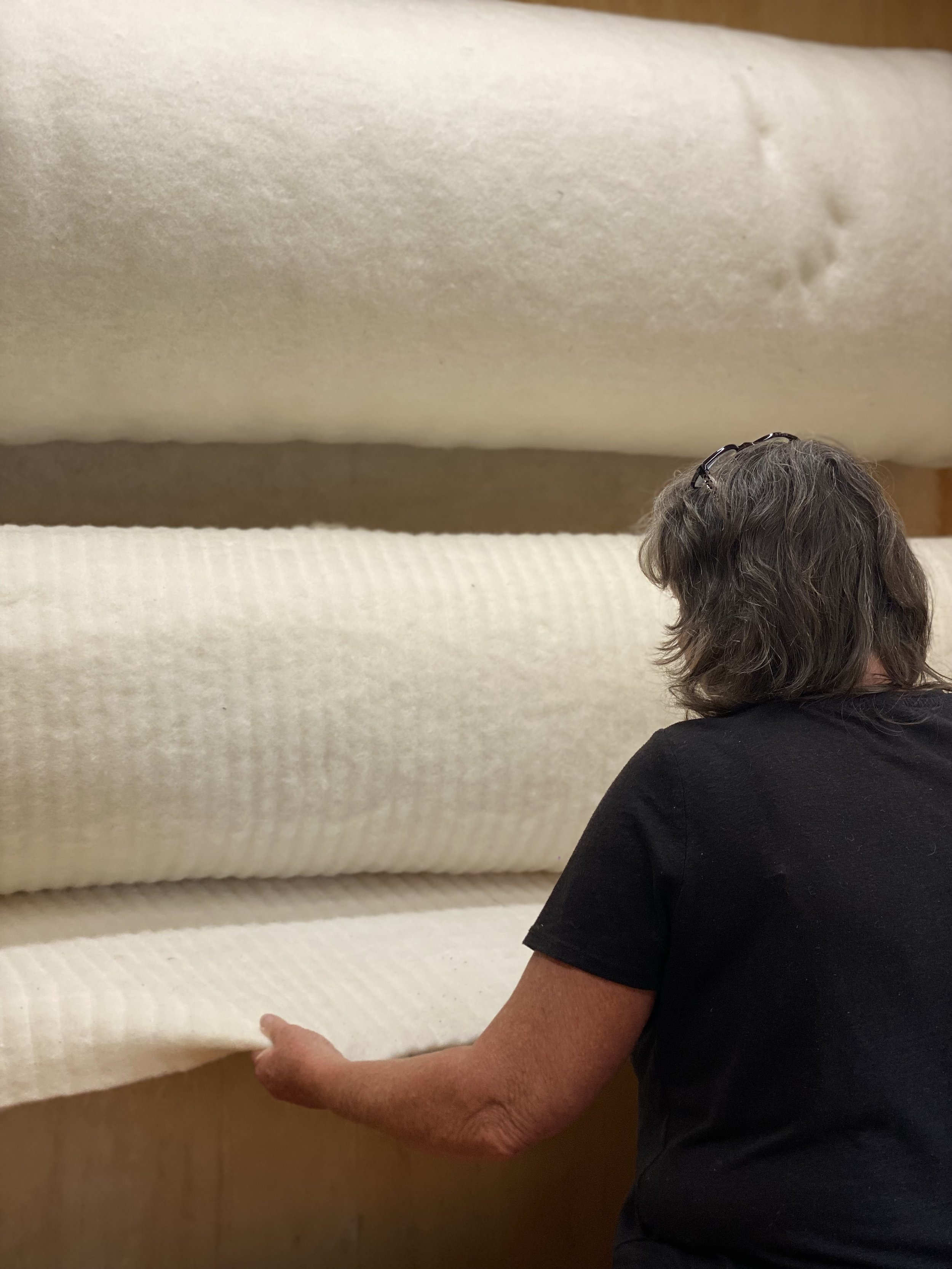 A woman with gray hair and glasses on her head is examining or touching large white rolls of fabric or material in a store or warehouse.