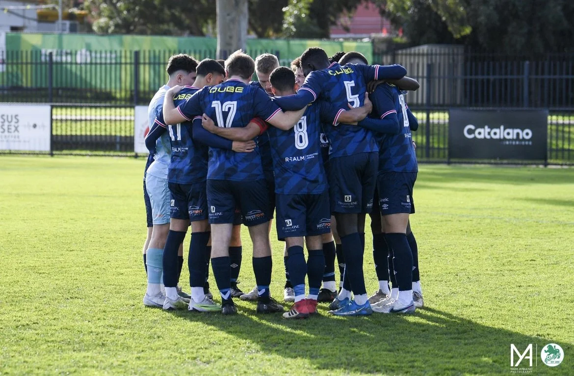 Soccer team huddled together in a circle on the field.