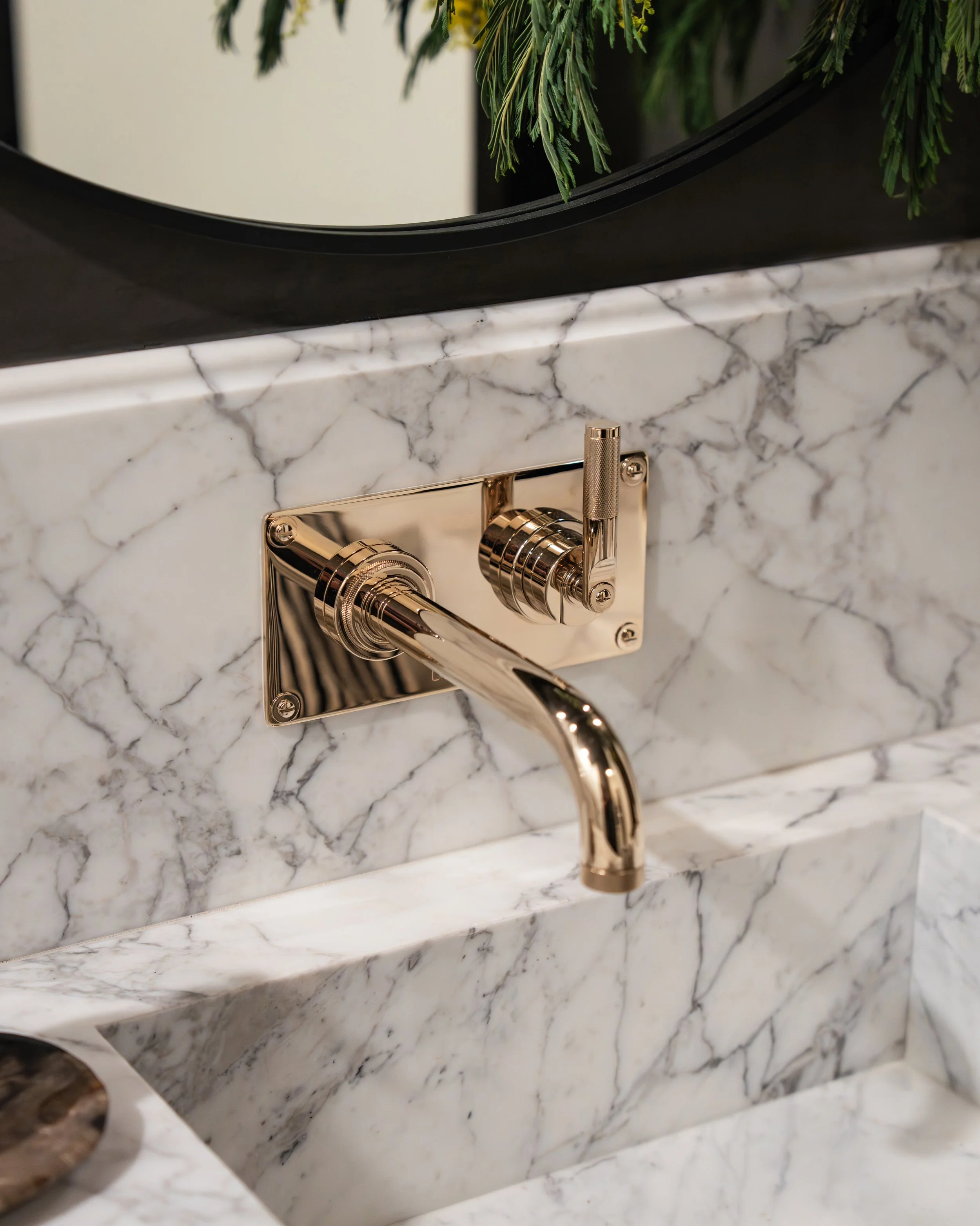Close-up of a gold-colored faucet and part of a marble countertop with a marble backsplash.