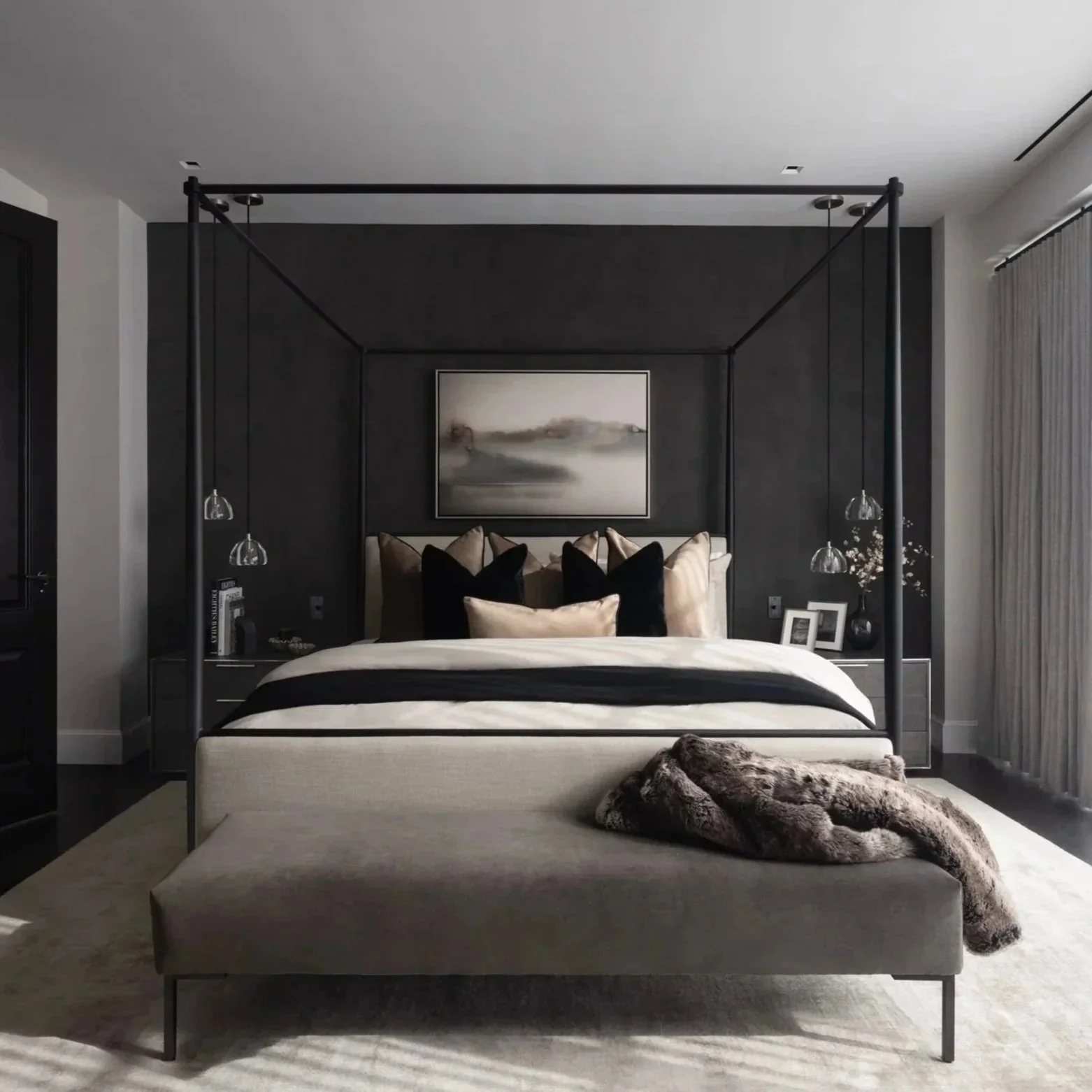 A modern bedroom with a four-poster bed with black and beige pillows, a textured fur blanket on the foot of the bed, a black accent wall with a landscape painting, hanging pendant lights on either side, and a beige bed frame with black trim. There are two picture frames and a small flower arrangement on the right side of the bedside table, and a curtain is drawn to the right.