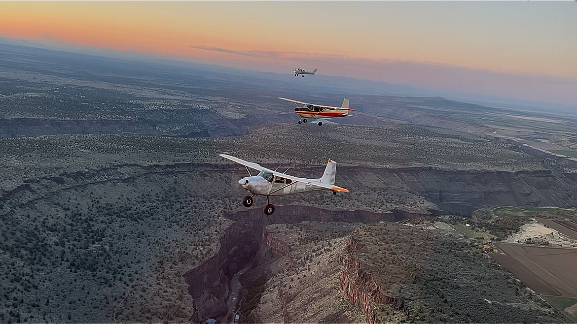 Single-engine airplane flying over canyon landscape at sunset during flight training