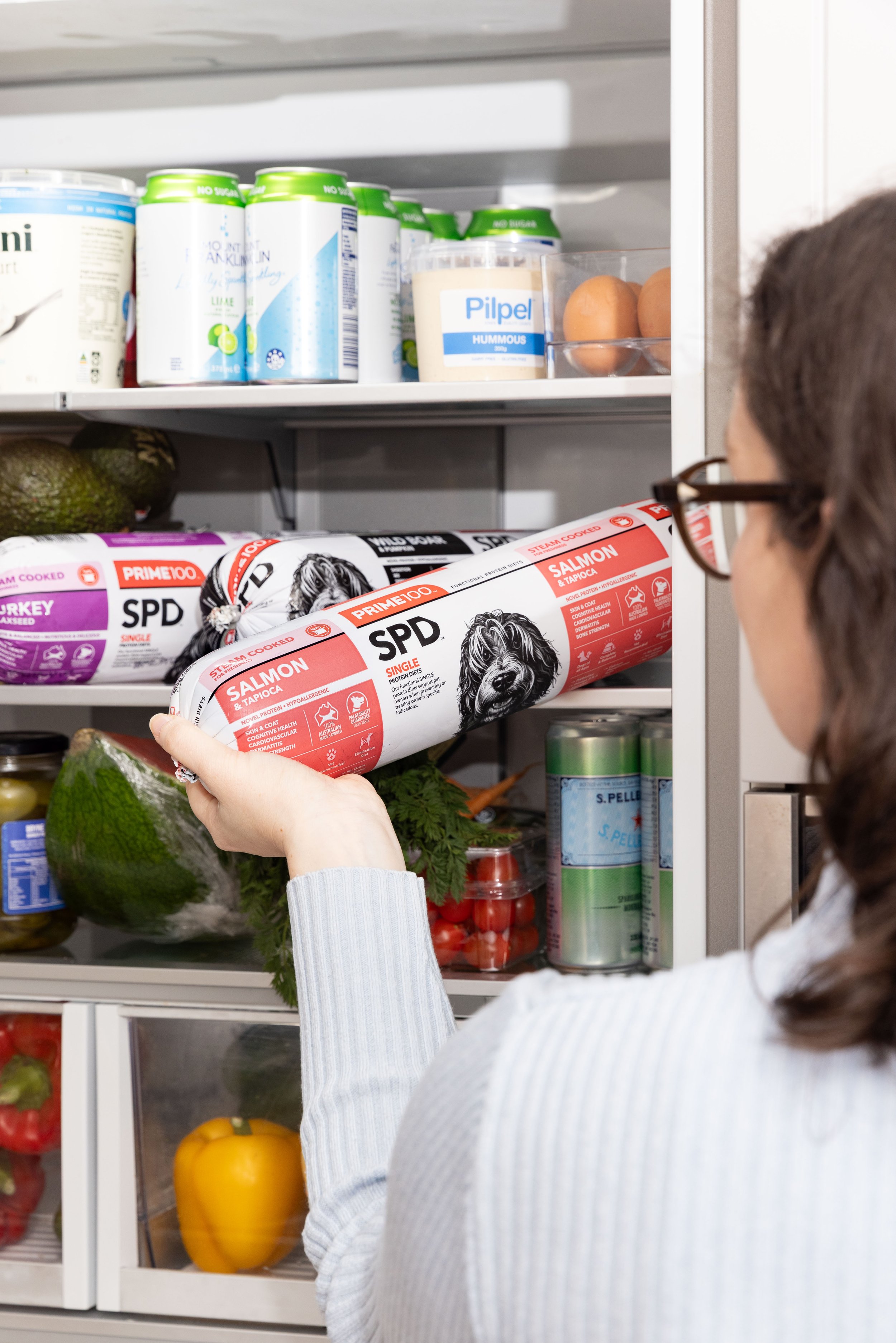 Woman holding a canned salmon dog food inside a refrigerator.