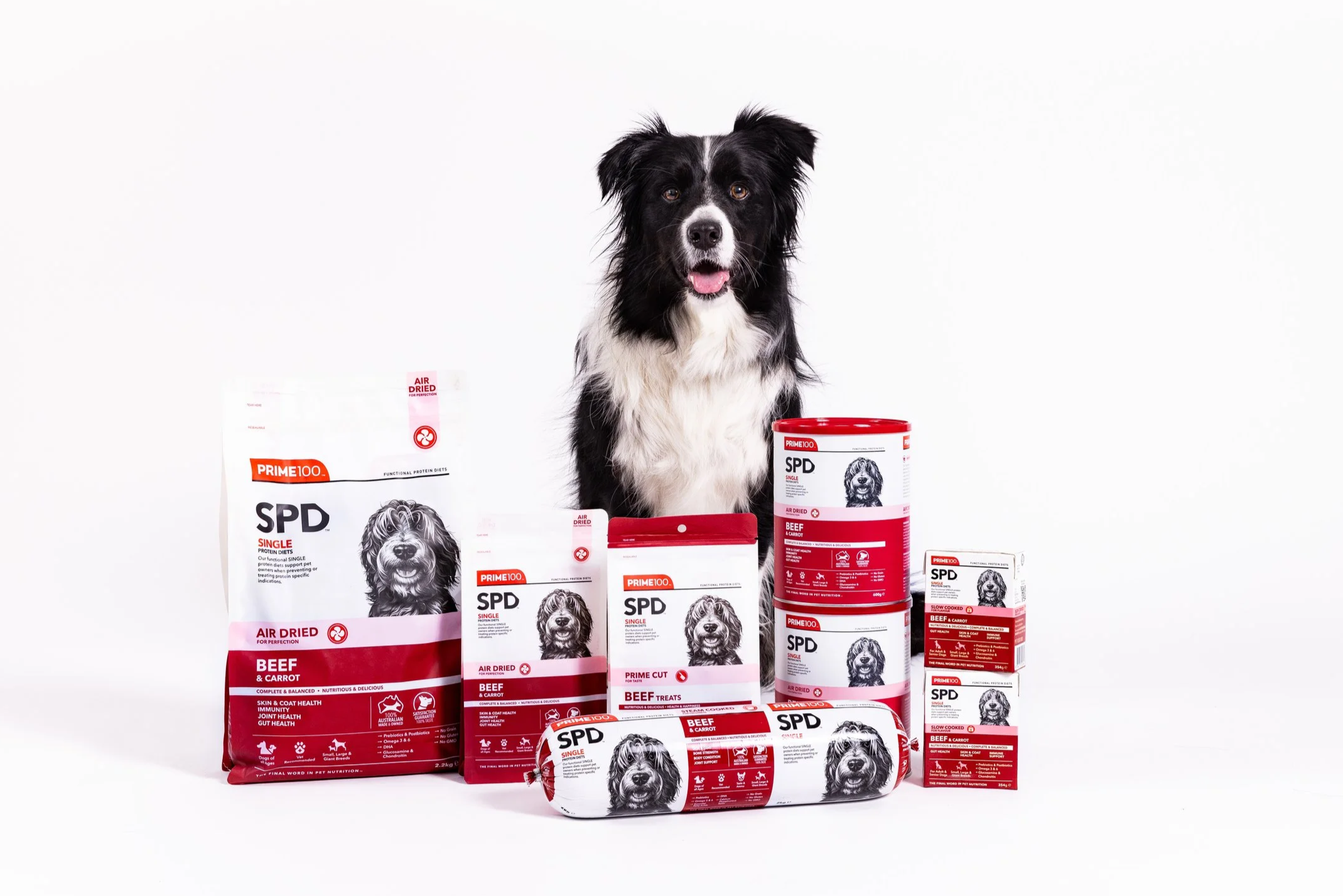 A black and white dog sitting behind various packages of dog food and treats on a white background.