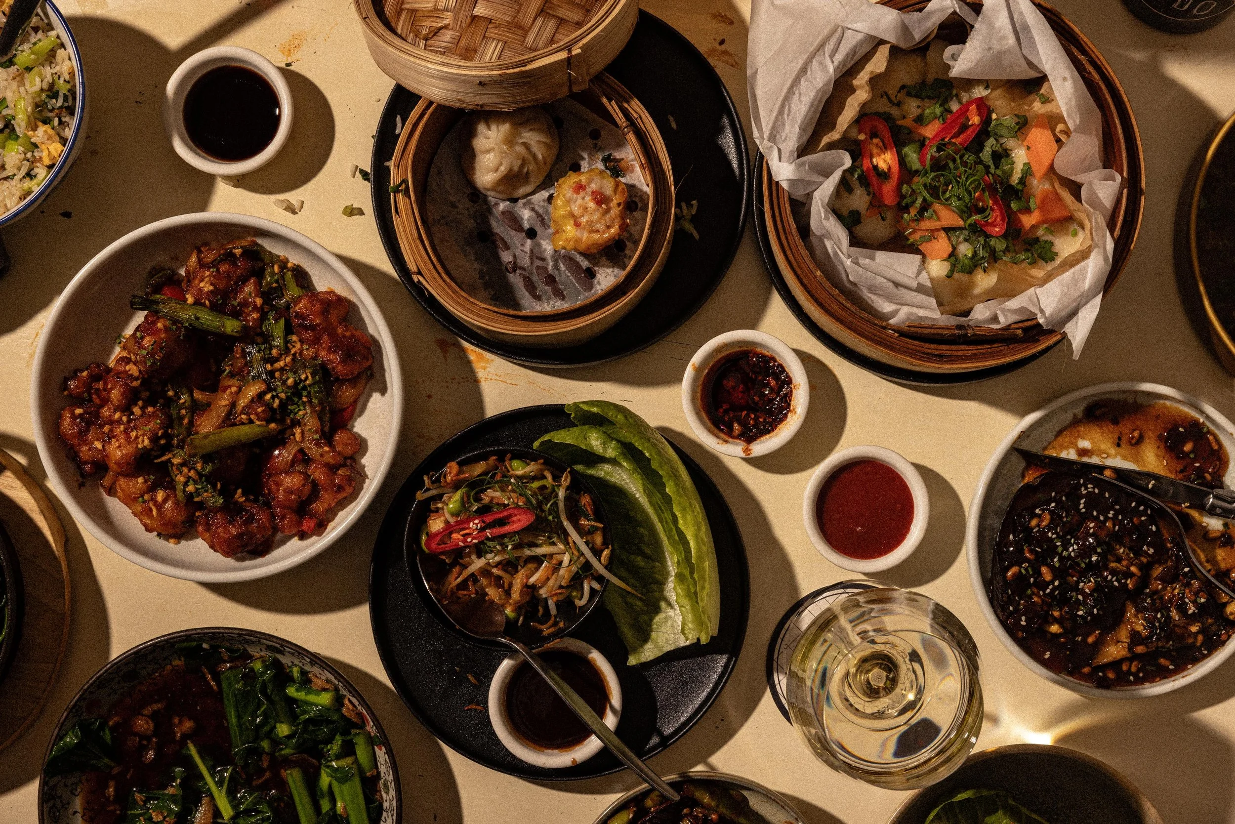 A top-down view of a table filled with various Asian dishes including dumplings, stir-fried vegetables, and sauces.