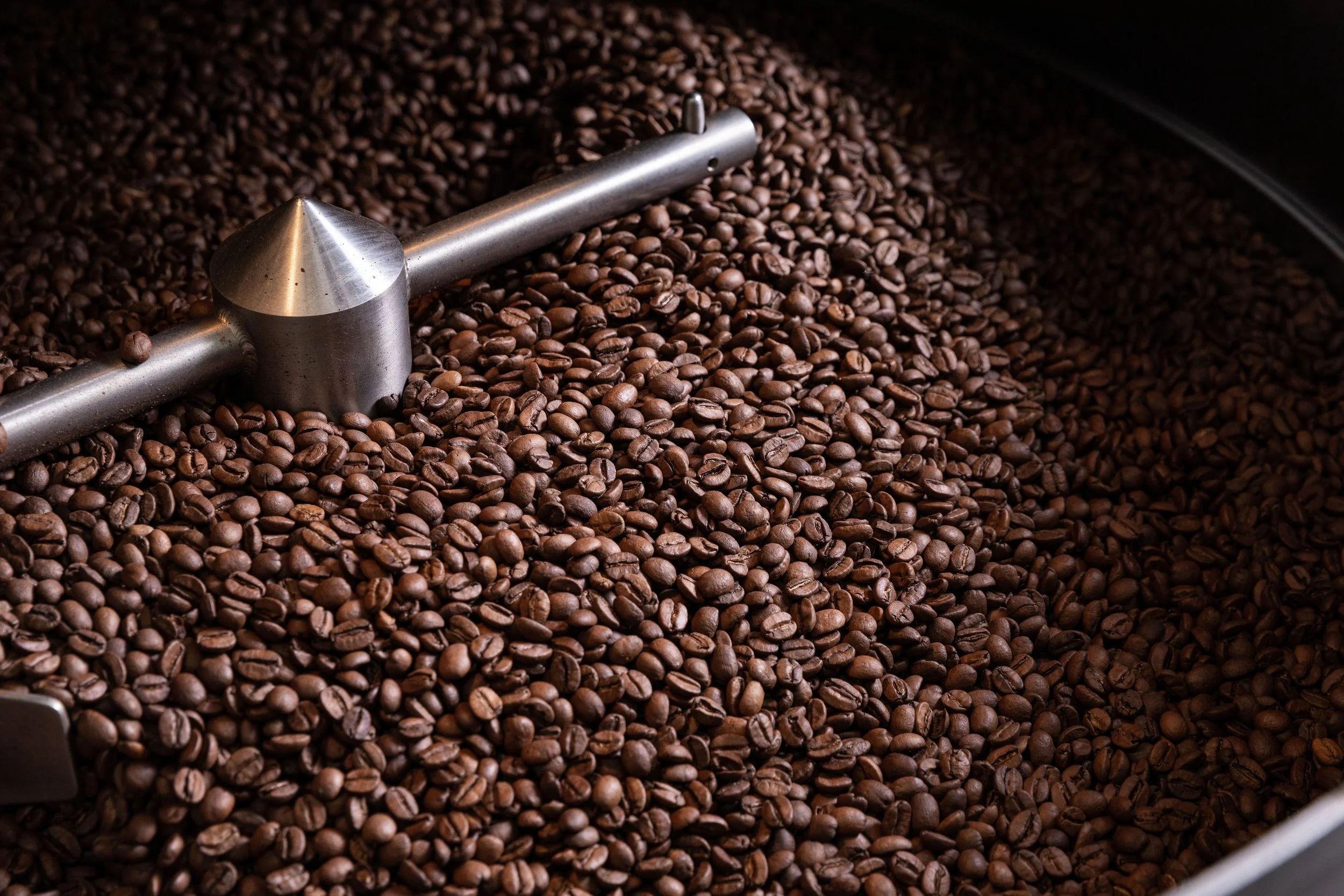 Close-up of roasted coffee beans in a roasting drum with a metal arm and spinner.