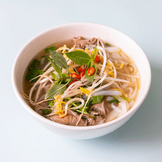 Bowl of Vietnamese pho with beef, bean sprouts, basil, sliced chili peppers, and green onions in broth