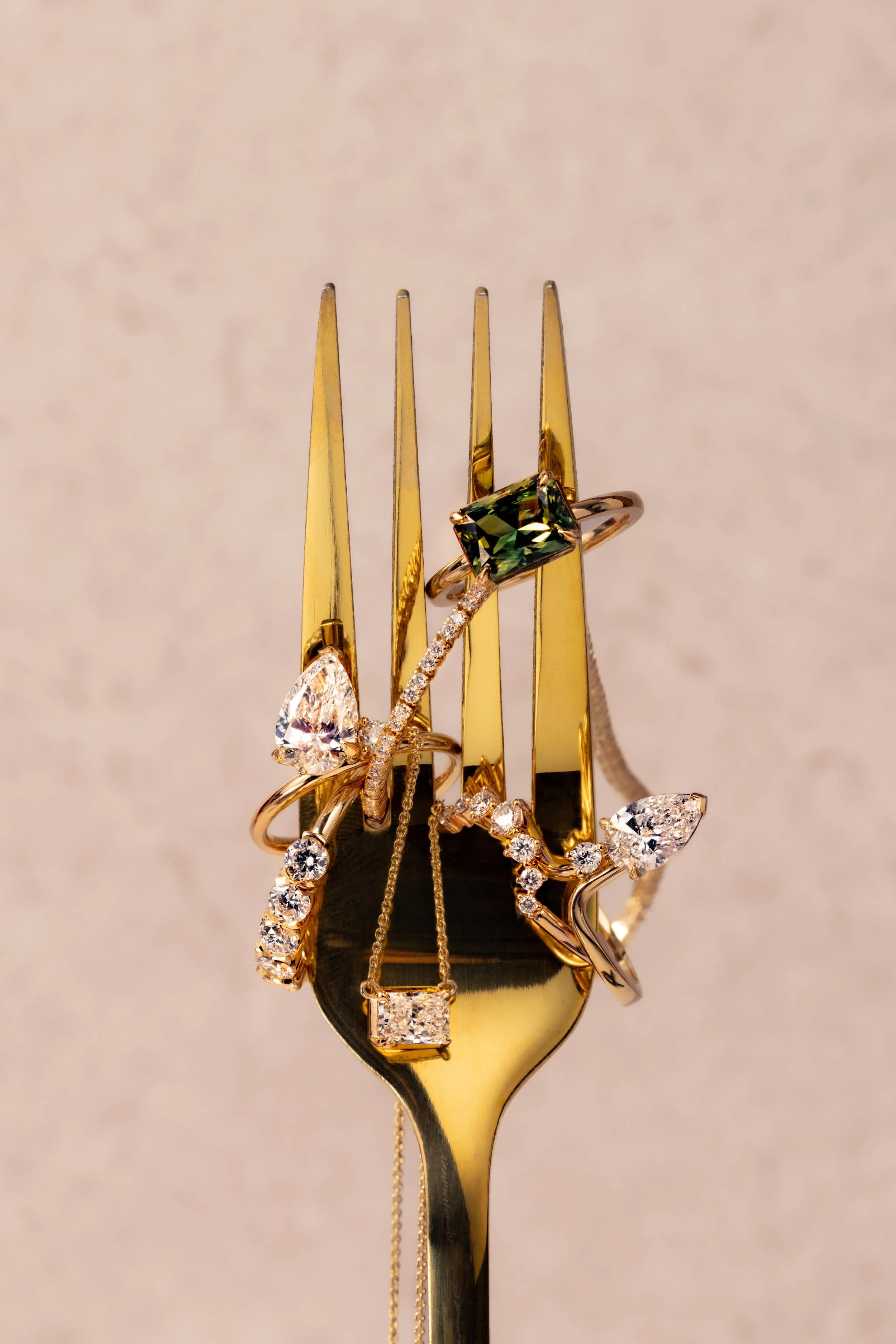 Gold fork with multiple diamond and gemstone rings, including a green gemstone ring and a diamond necklace, arranged on the tines.
